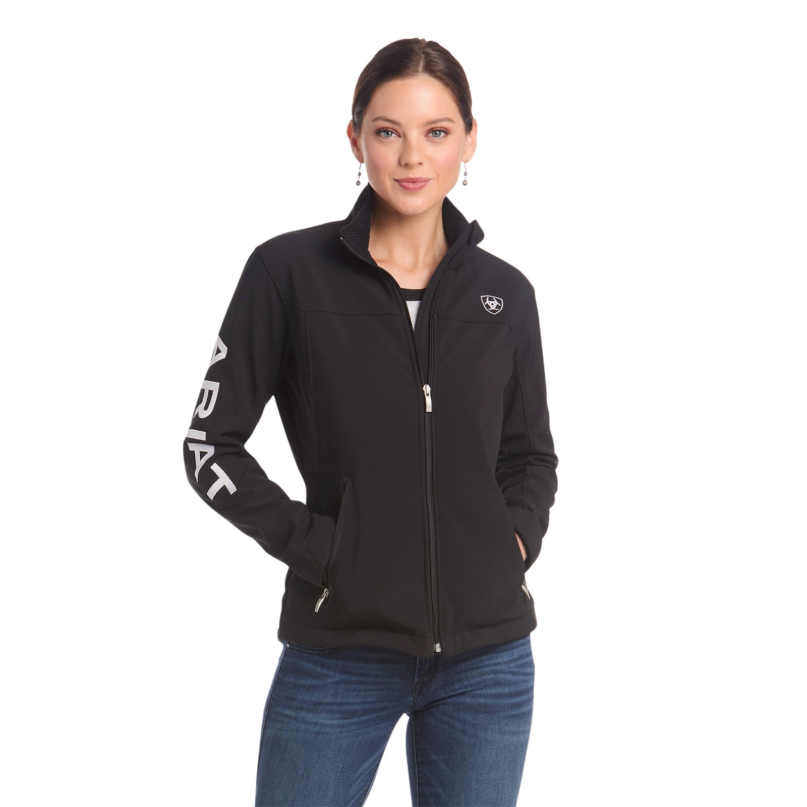 Ariat Women's Team Softshell Jacket. A woman wearing a black Ariat women's team softshell jacket with colorblock detailing, a standing collar, and zippered hand pockets.