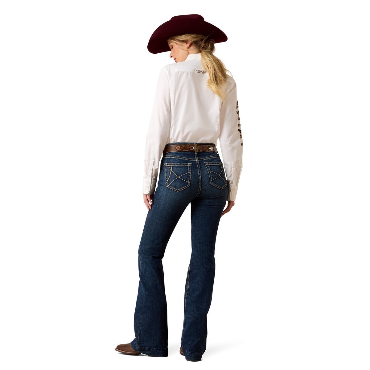 A woman shown from the back wearing a white western-style long-sleeve shirt with decorative stitching on the sleeve, dark blue flared jeans, a brown belt, and a dark red cowboy hat, against a plain white background.