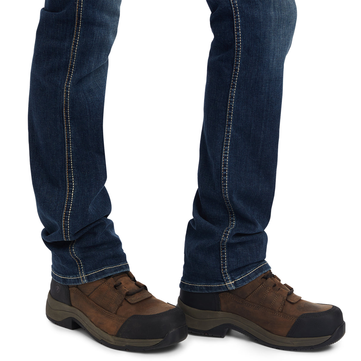 Brown shoes with black soles worn with blue jeans on a white background
