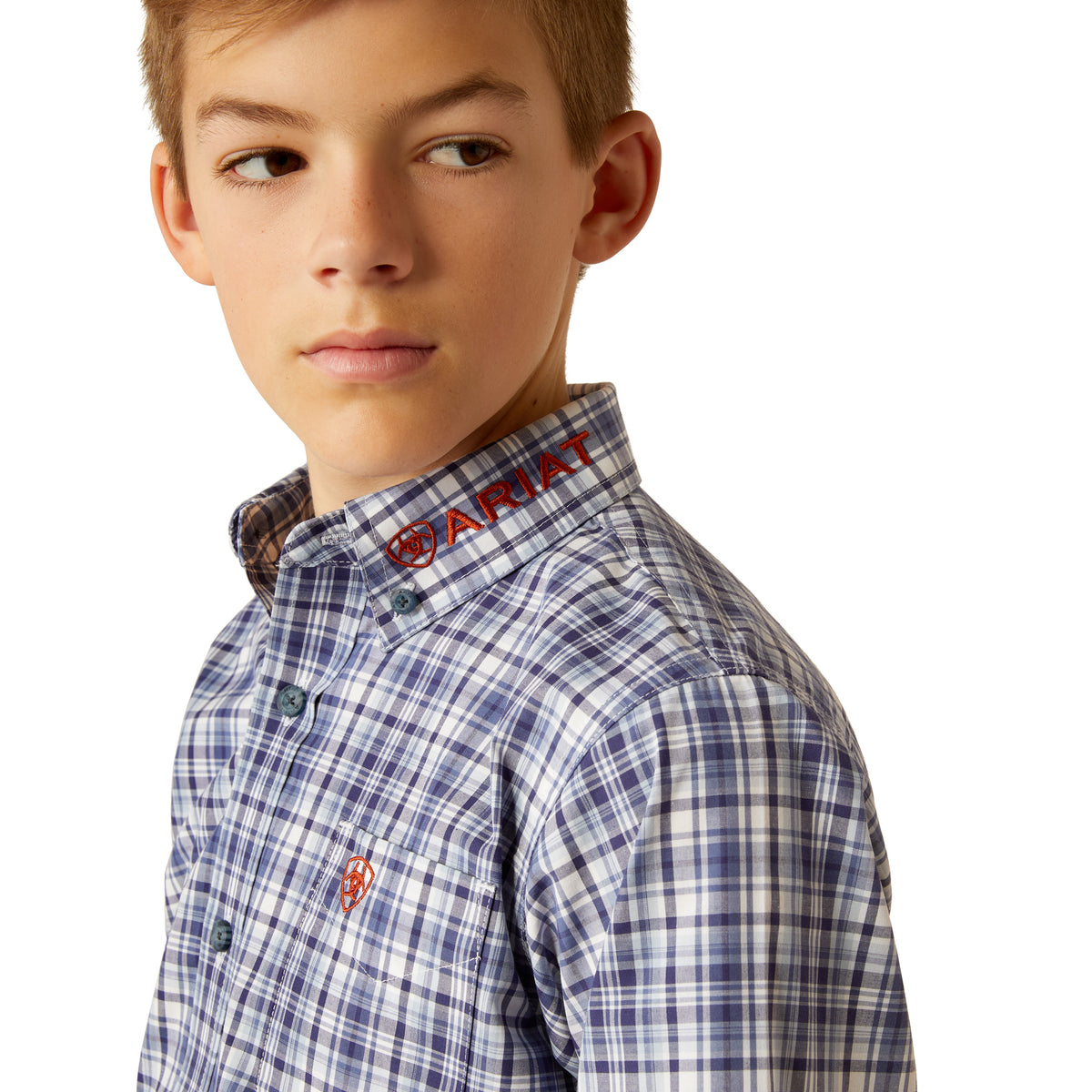 Ariat Boy's Pro Series Team Orion L/S Western Shirt. Close-up of a boy wearing a blue plaid shirt with a logo on the collar.