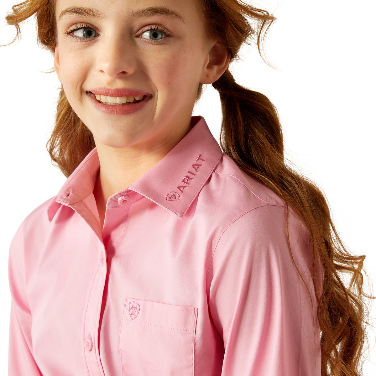 Ariat Girl's Team Kirby L/S Western Shirt. Person wearing a pink shirt with a logo on a white background