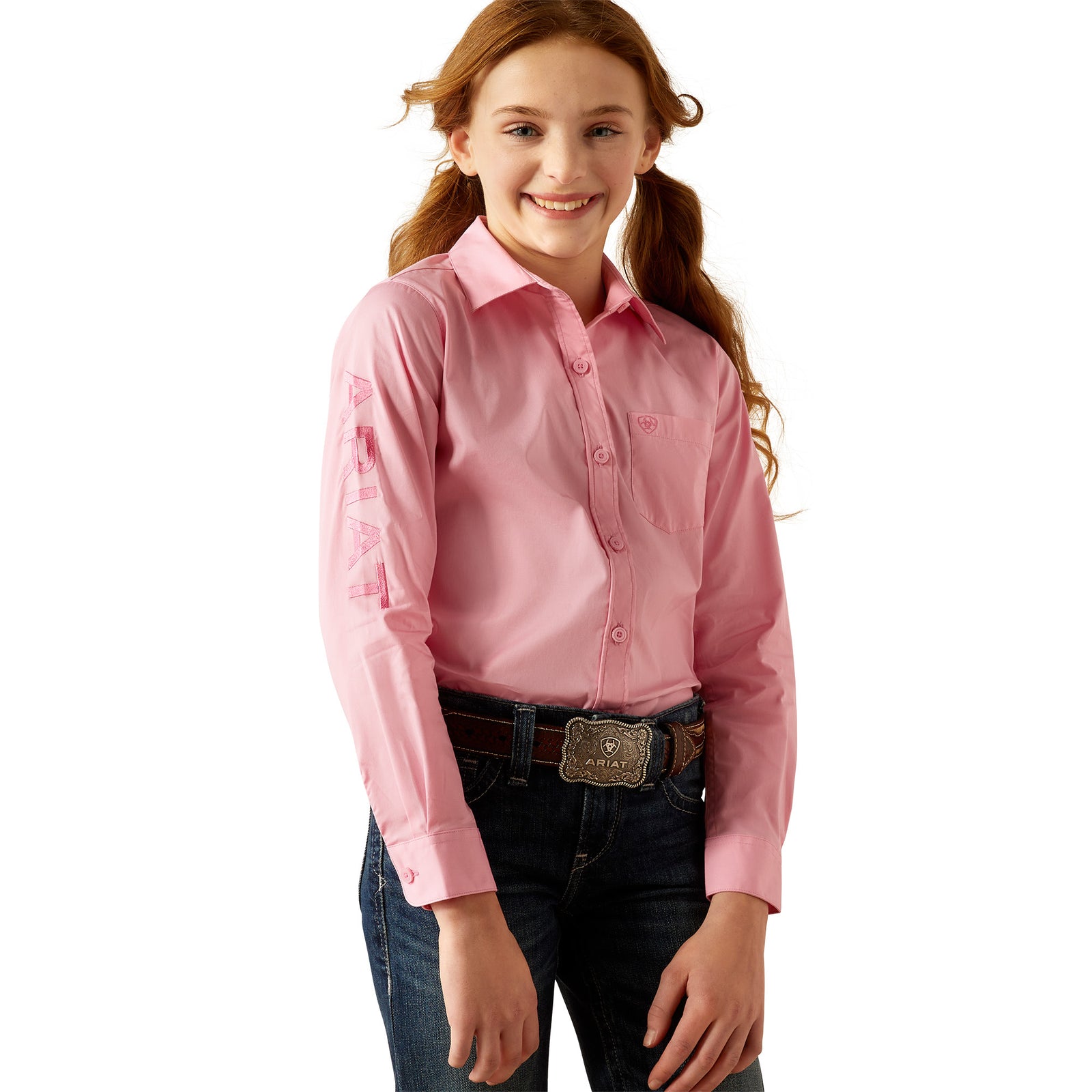 Ariat Girl's Team Kirby L/S Western Shirt. A girl wearing a long-sleeved pink Western shirt with a collar, button-up front, and she is smiling.