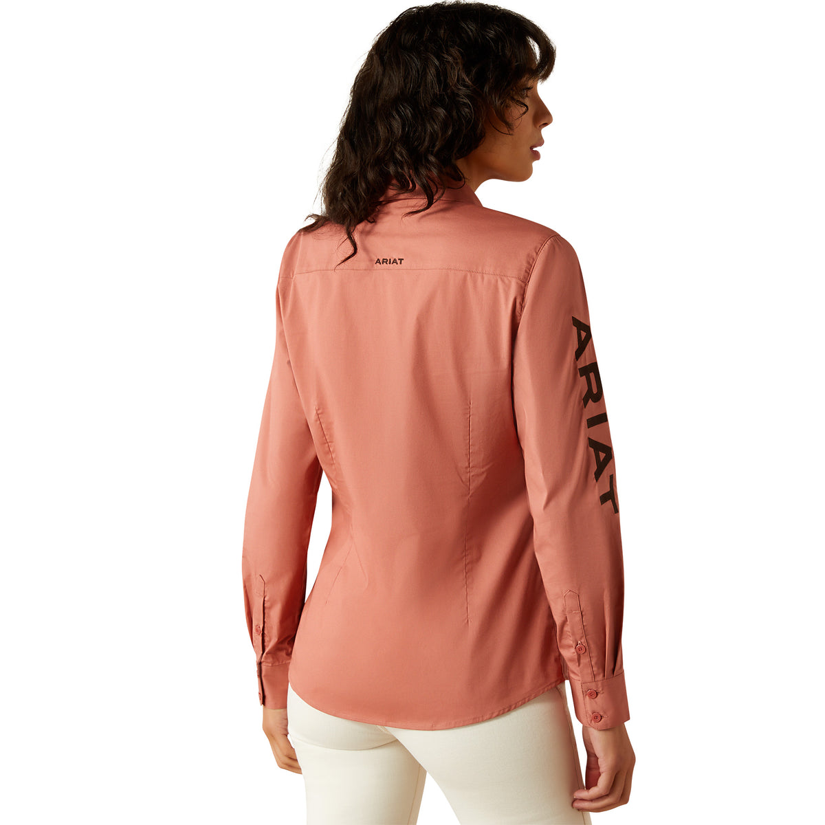 Ariat Women's Wrinkle Resistant Team Kirby L/S Western Shirt. Person wearing a pink long-sleeve shirt with branding on the sleeve.