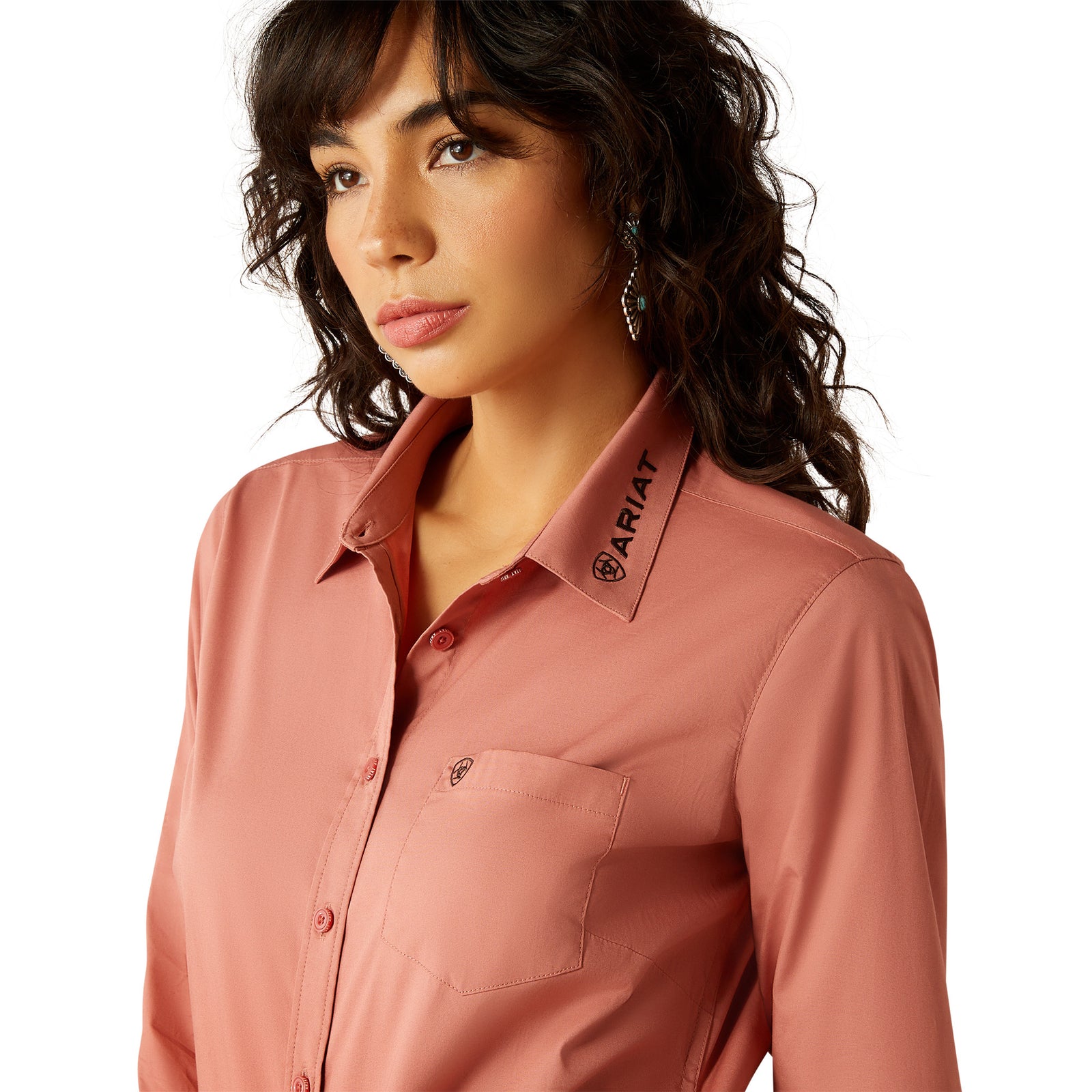 Ariat Women's Wrinkle Resistant Team Kirby L/S Western Shirt. Woman wearing a pink shirt with a brand label visible.