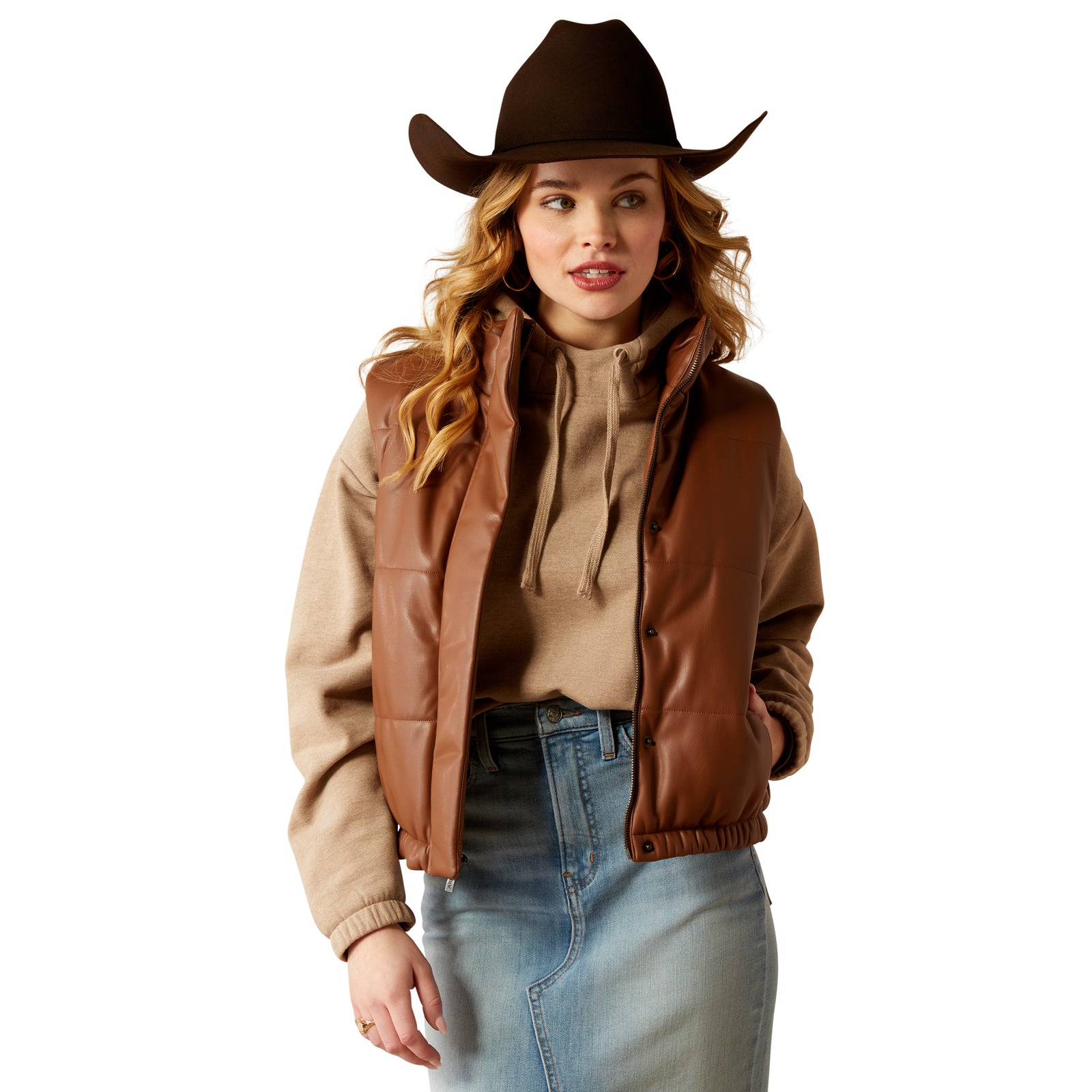 Ariat Women's Swirls Faux Leather Vest. A woman wearing a brown faux leather vest, a beige top, blue jeans, and a brown cowboy hat.