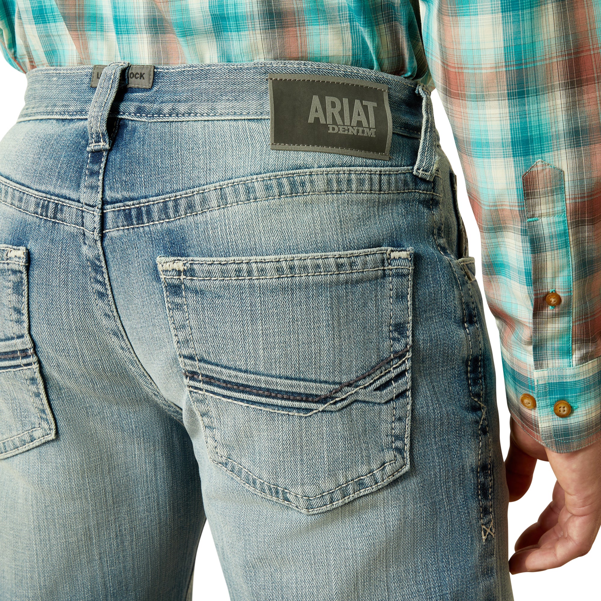 Ariat Men's M4 Thomas Relaxed Boot Cut Jean. Person wearing blue jeans with Ariat logo, plaid shirt visible
