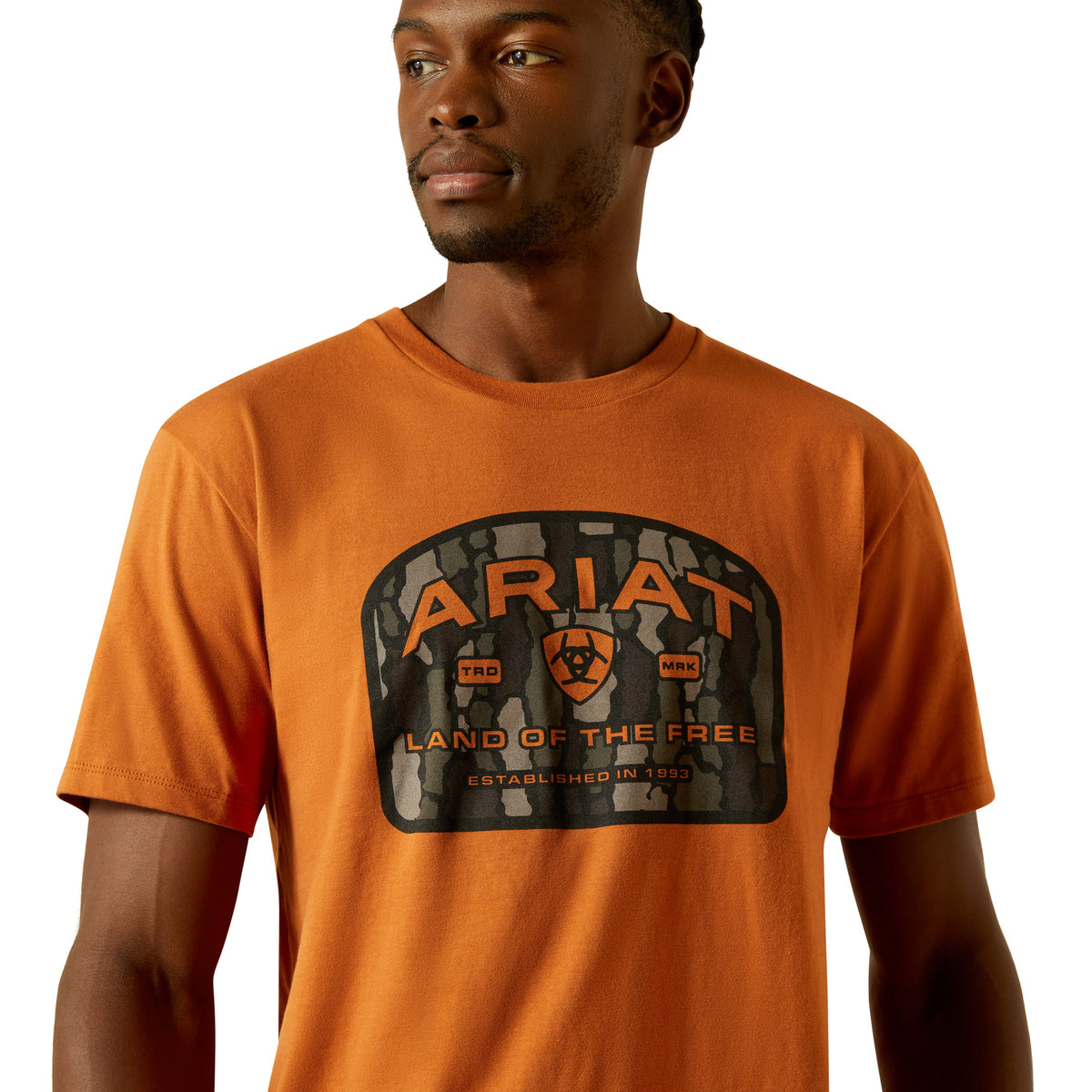 Ariat Men's Underlands Camo Badge T-Shirt. Man wearing an orange Ariat t-shirt with a logo on a white background