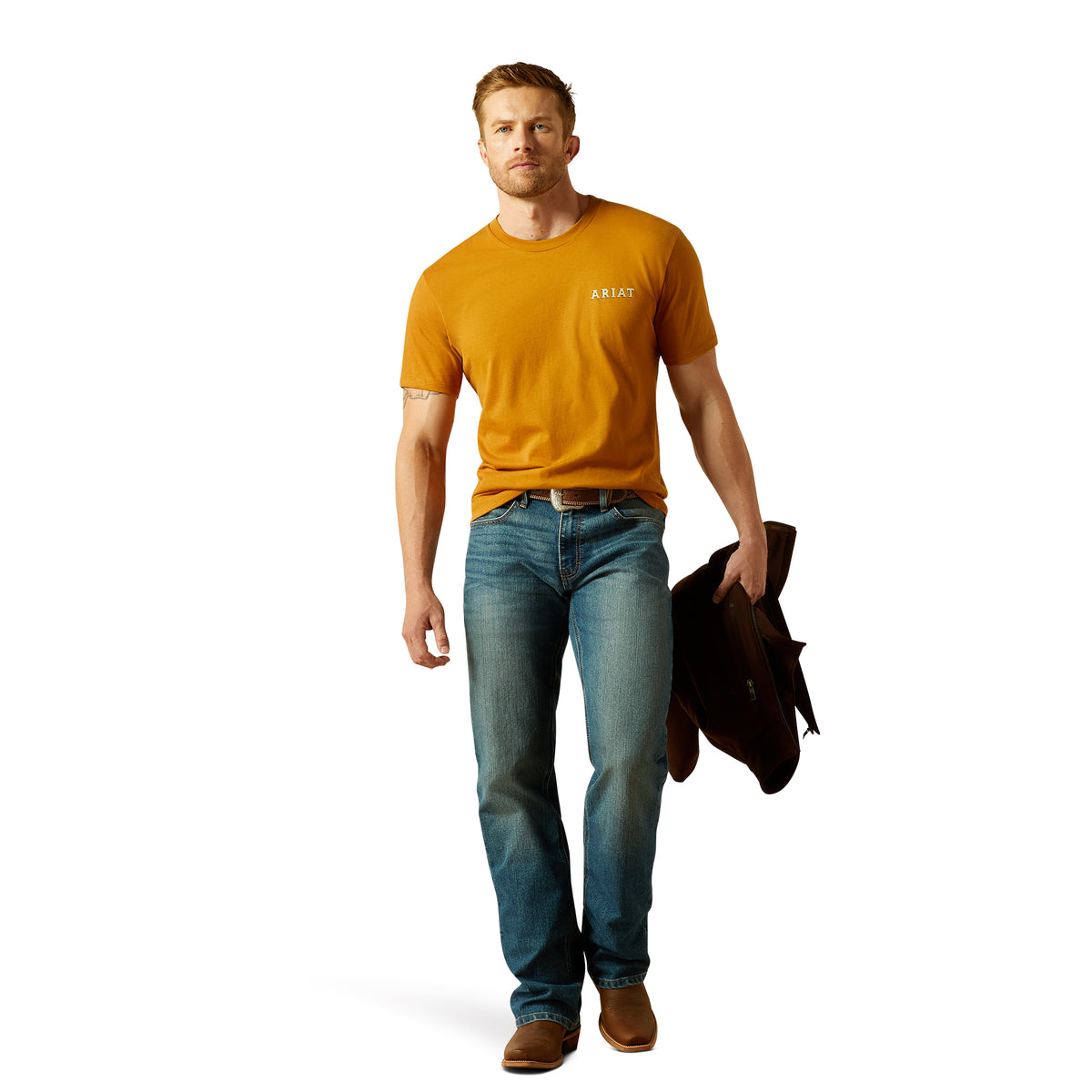 Ariat Men's Scorpion Seal T-Shirt. Man wearing a mustard yellow t-shirt and blue jeans holding a black jacket on a white background