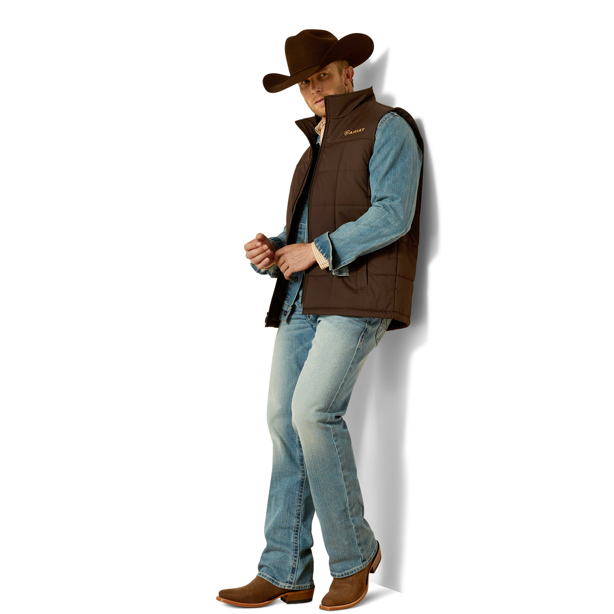 Man wearing a brown vest, blue jeans, and a cowboy hat on a white background
