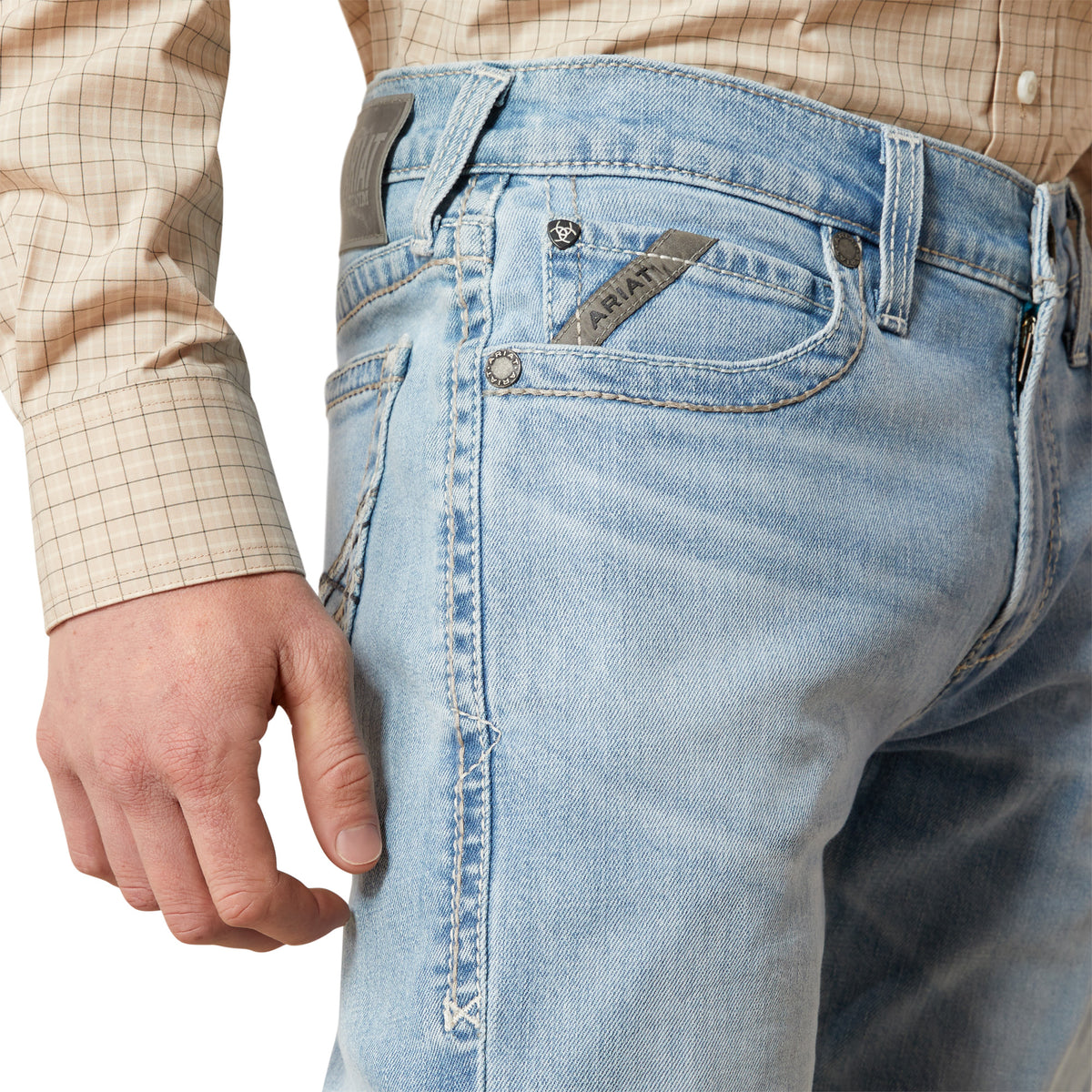 Close-up of light blue jeans with a brand logo, worn by a person.
