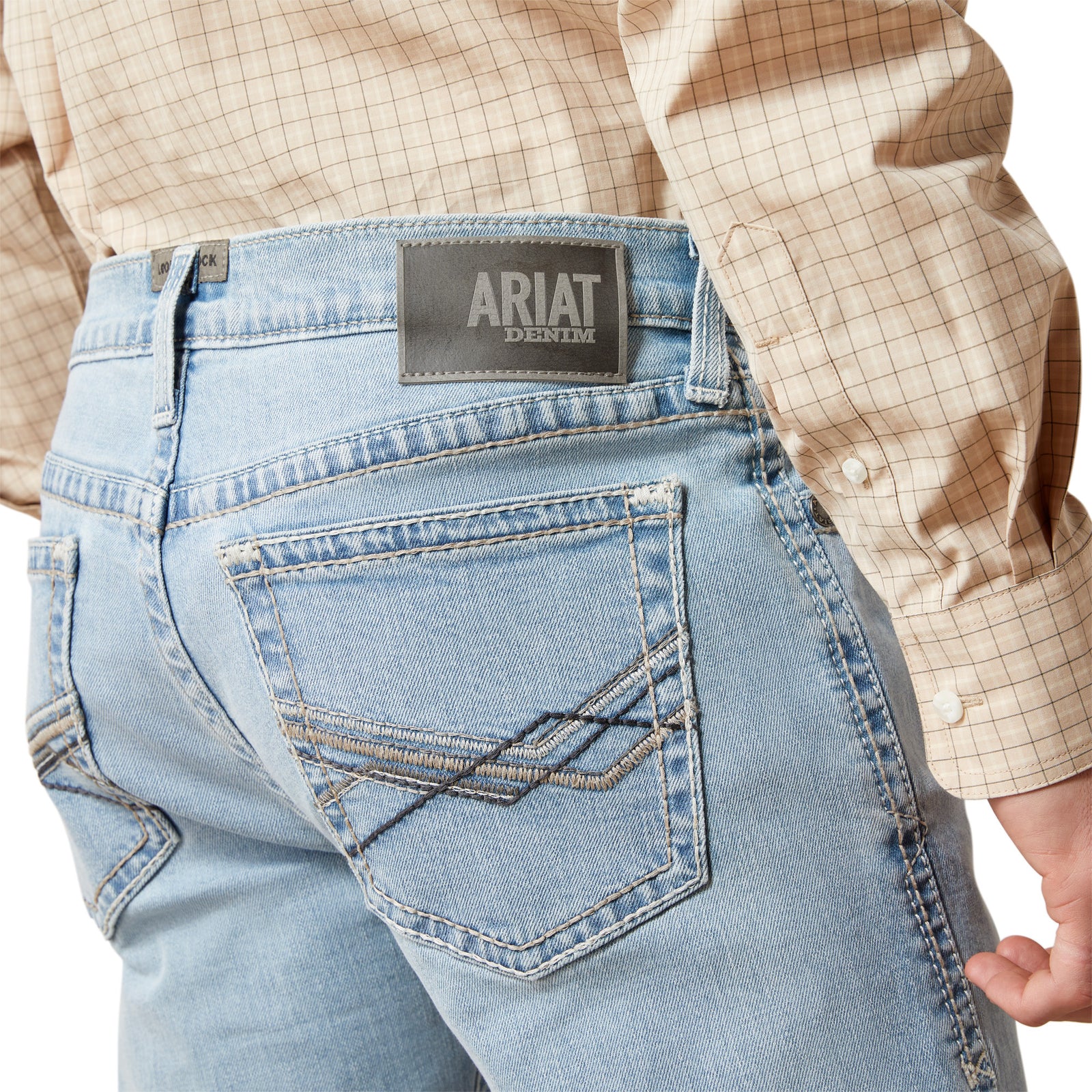 Close-up of blue jeans with Ariat logo on the back pocket, worn by a person.