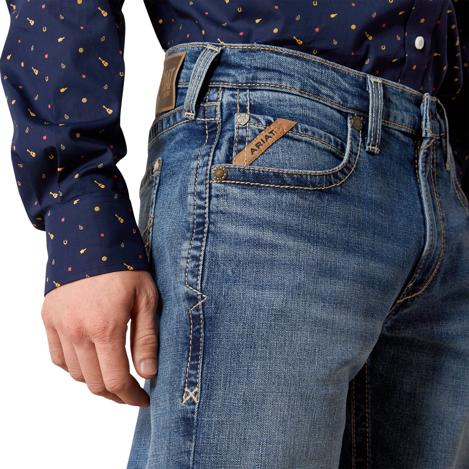 Close-up of blue jeans with a brand label, worn by a person wearing a patterned shirt.
