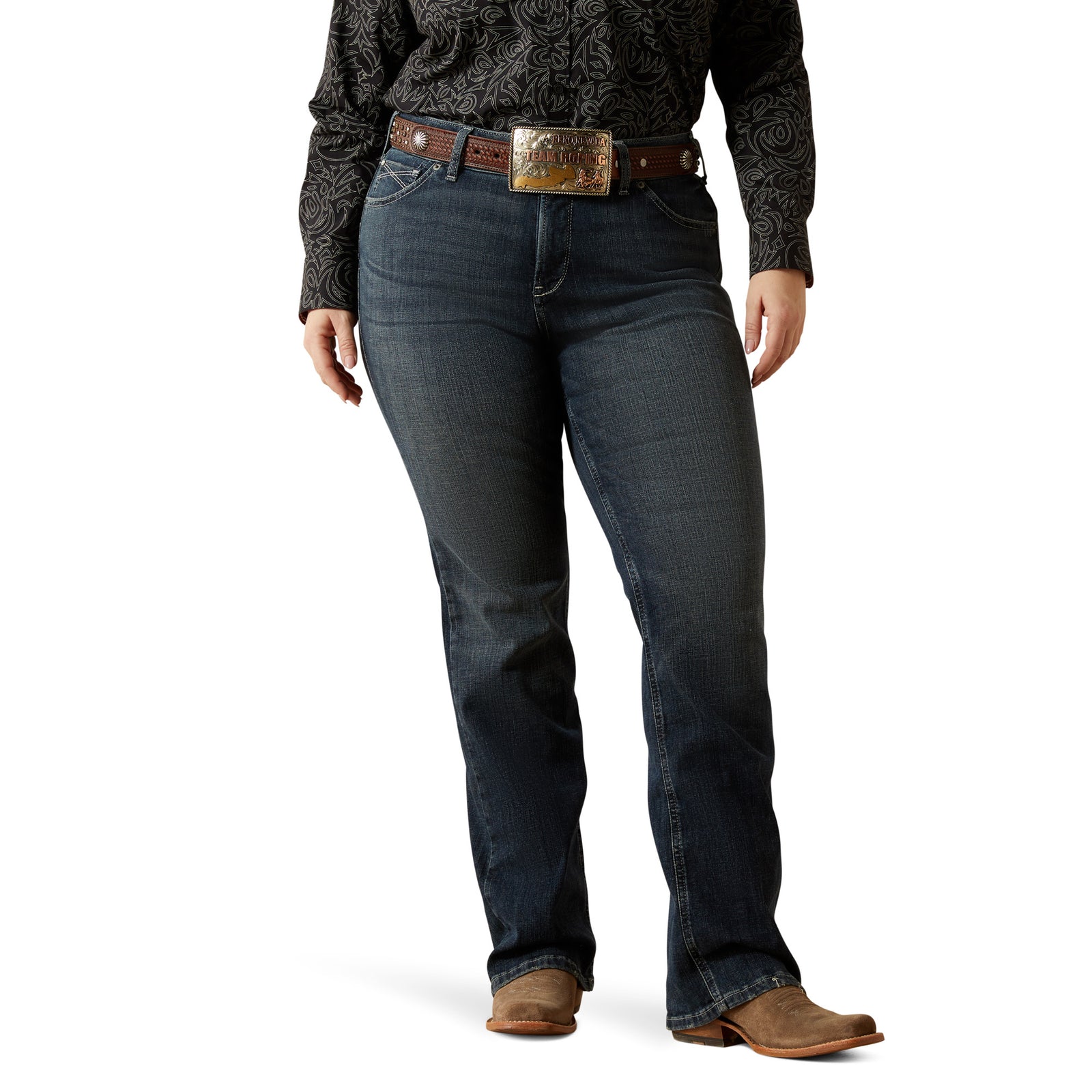 Ariat Women's Esti Perfect Rise Boot Cut Jean. Person wearing dark blue jeans with a patterned shirt and brown belt on a white background
