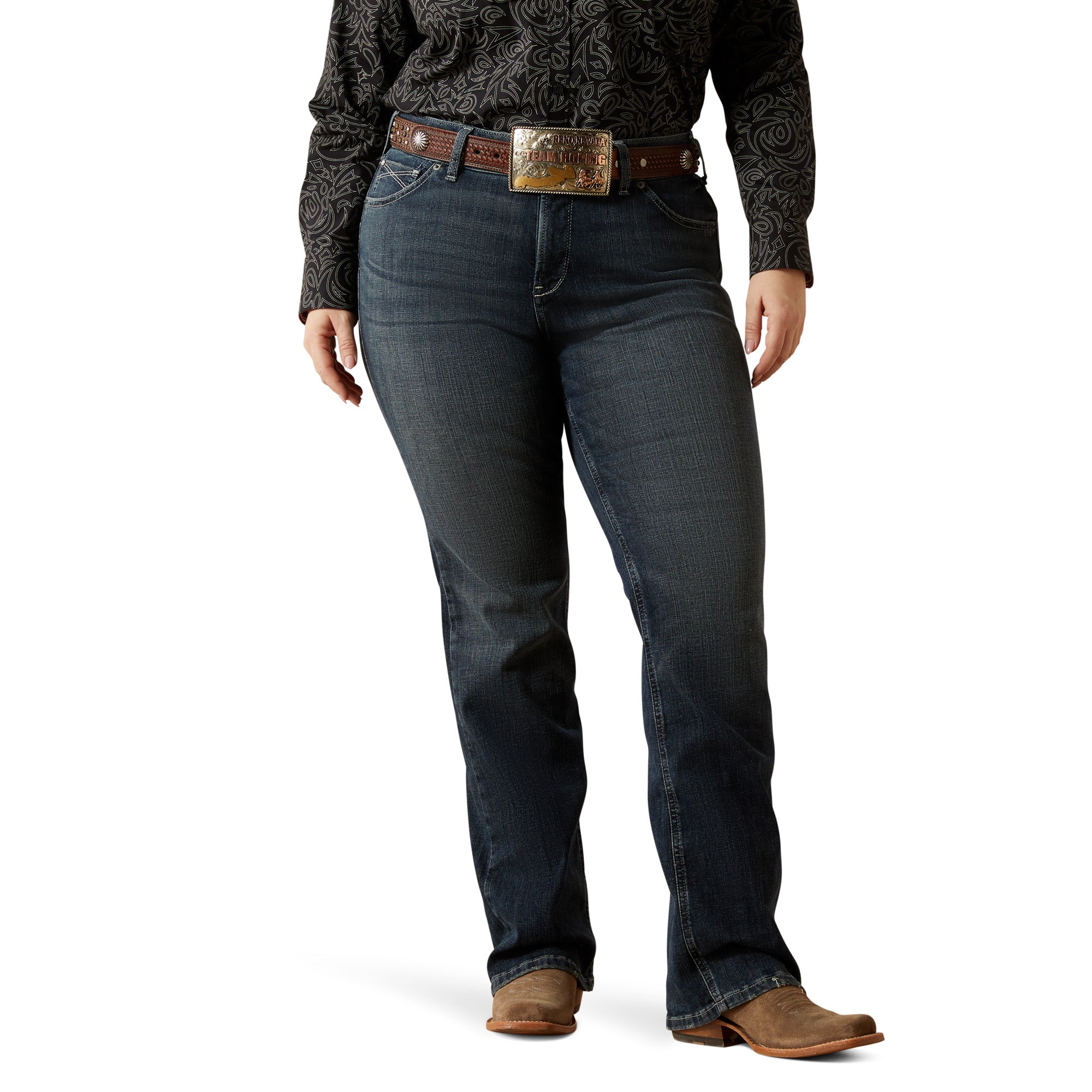 Ariat Women's Esti Perfect Rise Boot Cut Jean. Person wearing dark blue jeans with a patterned shirt and brown belt on a white background
