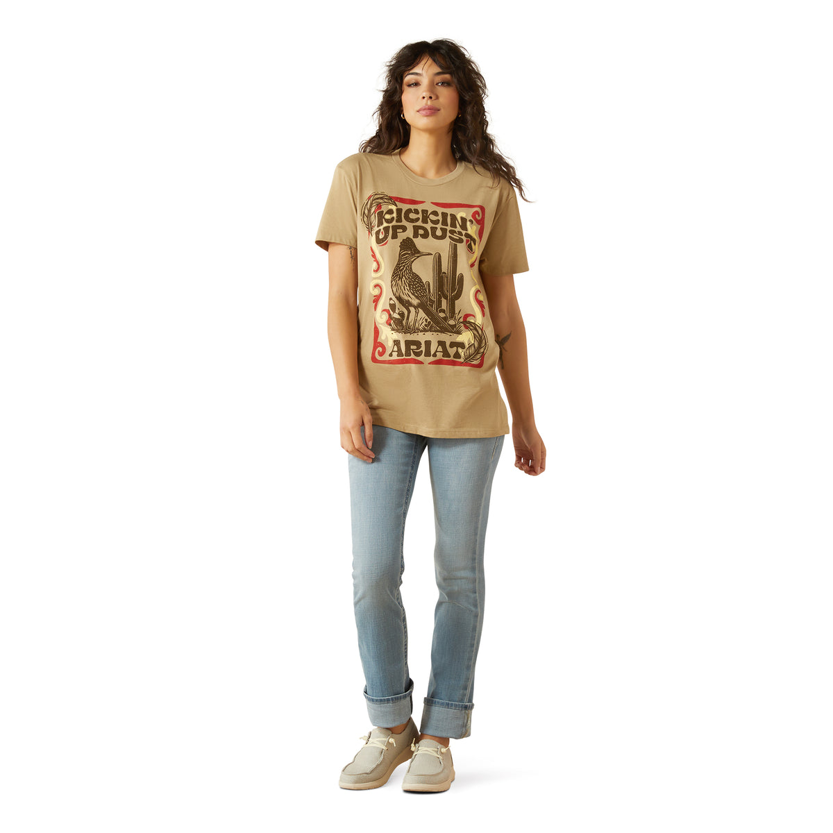 Ariat Women's Kickin Up Dust T-Shirt. Woman wearing a beige t-shirt with graphic design and text, standing against a white background
