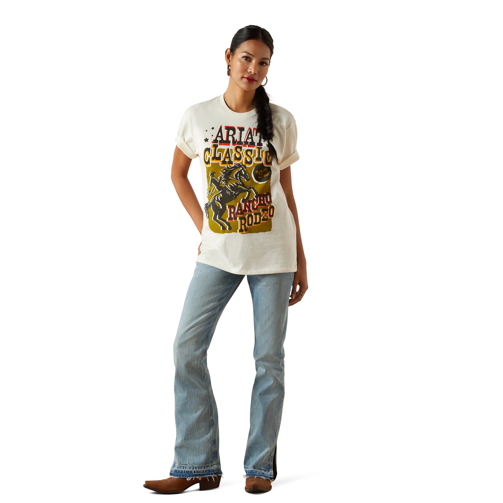 Ariat Women's Classic Rodeo T-Shirt. Woman wearing a white t-shirt with a graphic design and blue jeans on a white background