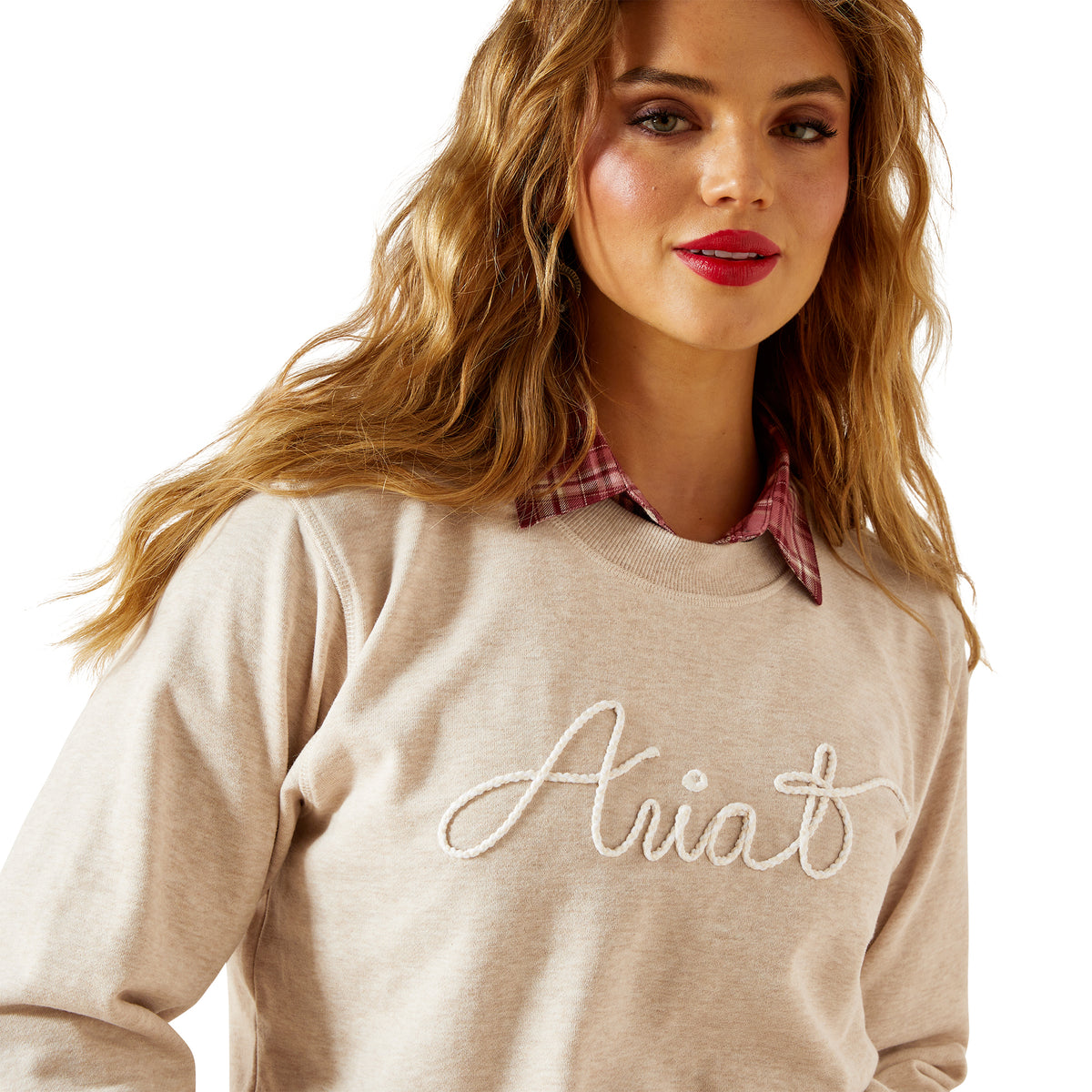 Woman wearing a beige sweater with 'Ariat' embroidery on a white background