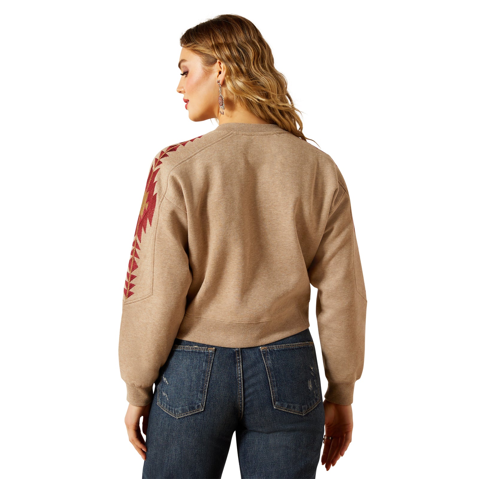 Woman wearing a beige sweater with red pattern on the back, standing against a white background