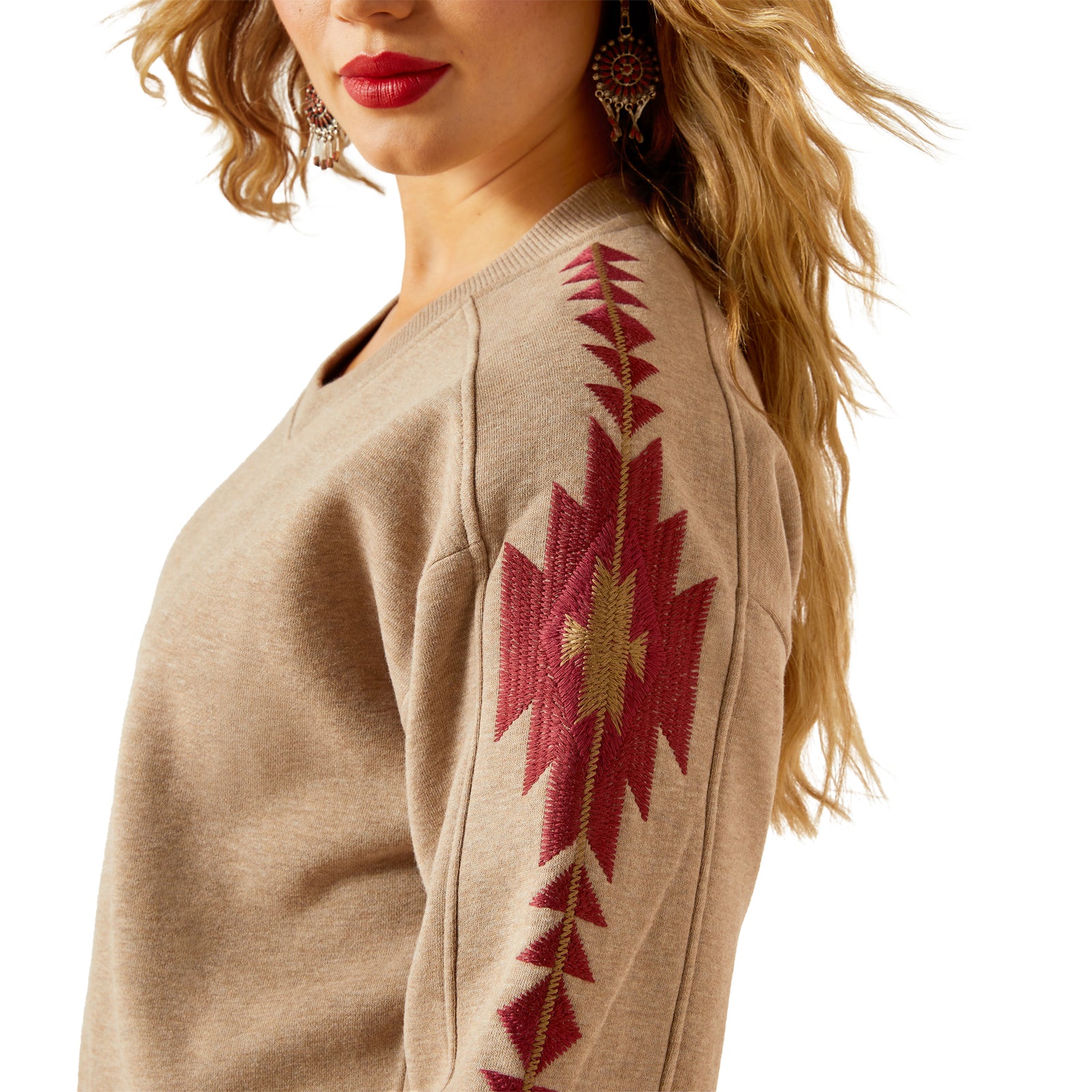 Beige sweater with red geometric pattern on sleeve, worn by a person.