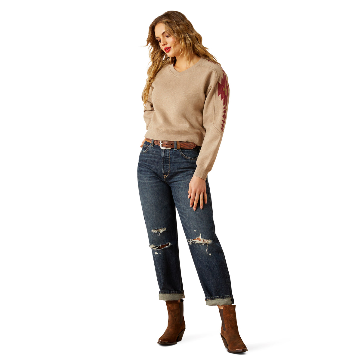Woman wearing a beige sweater with red accents, blue jeans, and brown boots on a white background