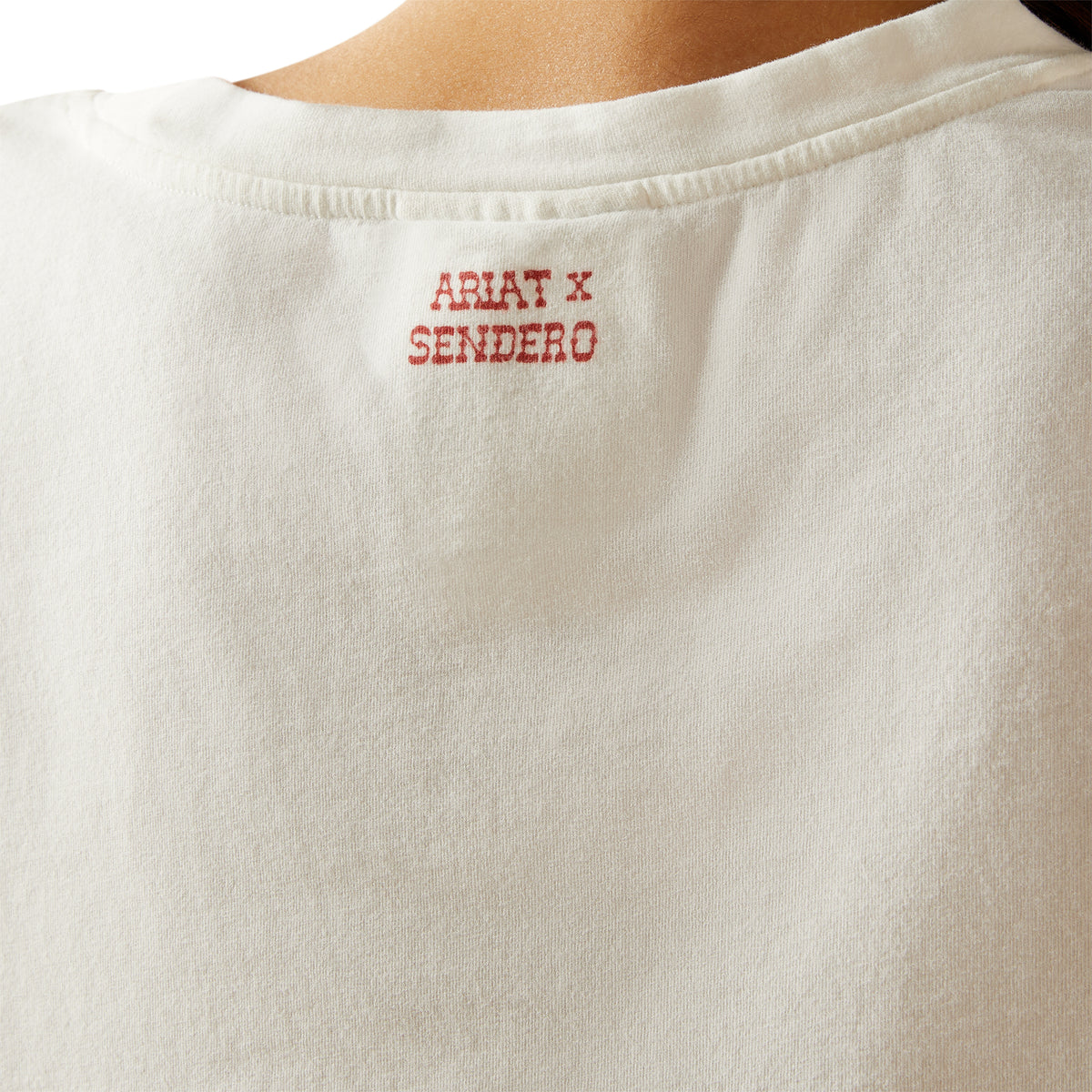 Ariat Women's Sendero Yeehaw S/S T-Shirt. Close-up of a white shirt with 'Ariat x Sendero' embroidery on a white background