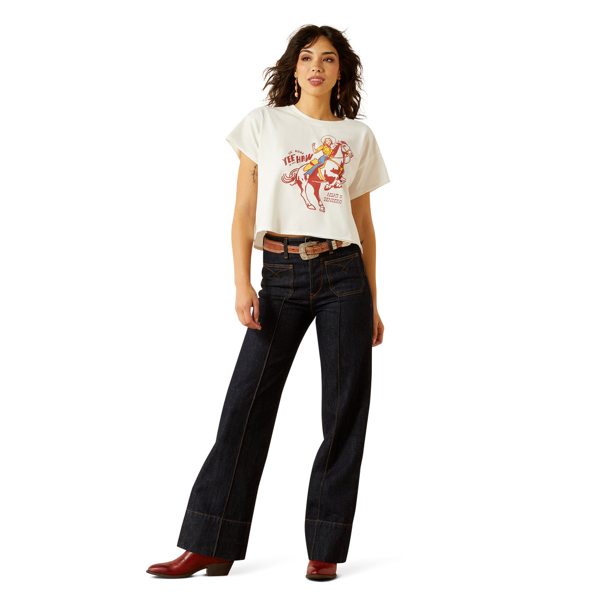 Ariat Women's Sendero Yeehaw S/S T-Shirt. Woman wearing a white t-shirt with a graphic design and dark jeans on a white background