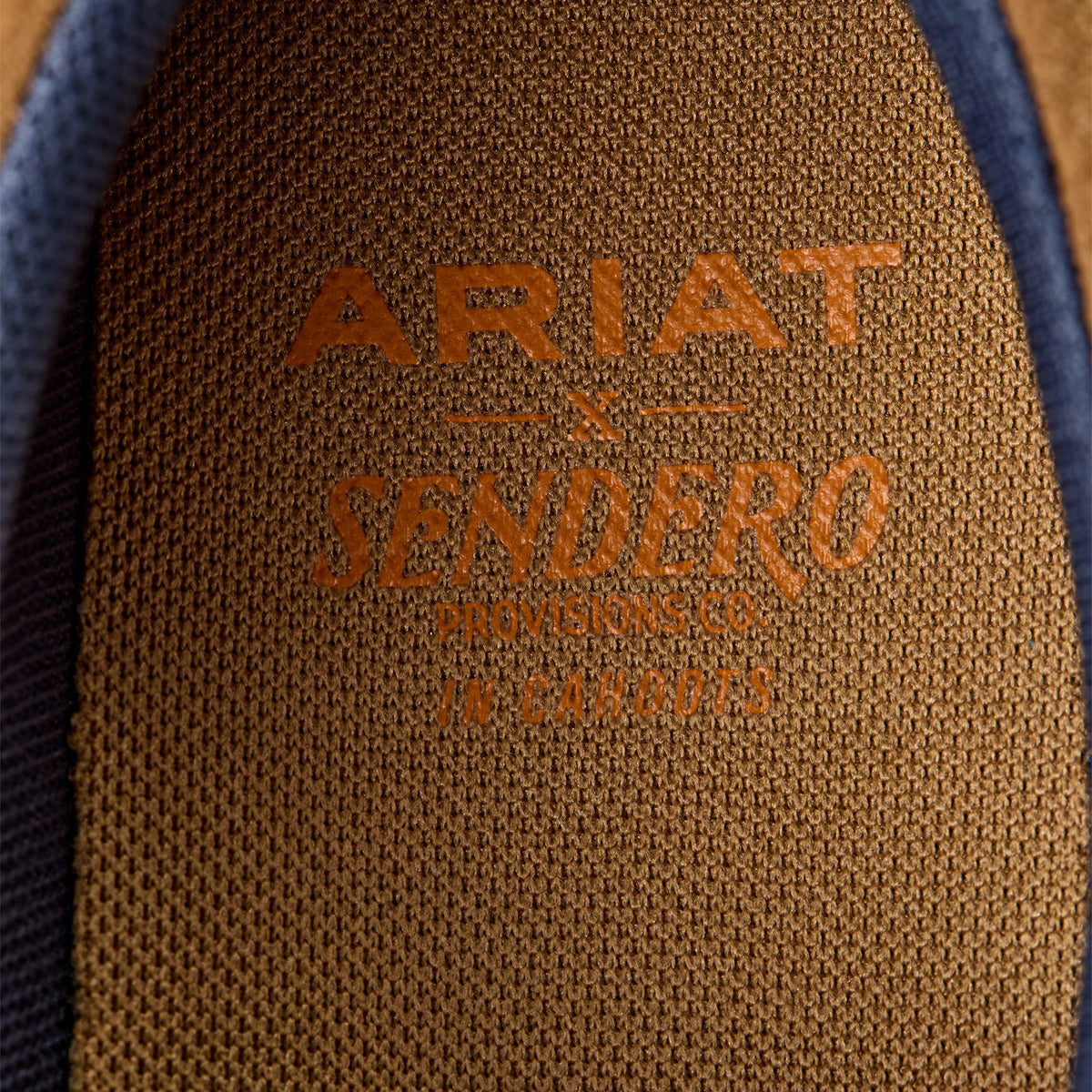 Ariat Women's Hilo Sendero Slip On Shoe. Close-up of Ariat Sendero logo on a brown textured surface