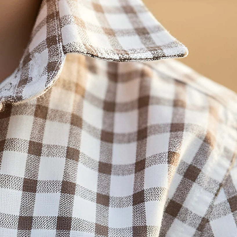 Young boy standing in a field wearing a checkered shirt and jeans.