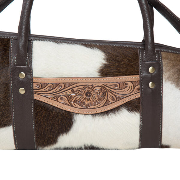 Handbag with cowhide leather and intricate tooled leather panel on a white background