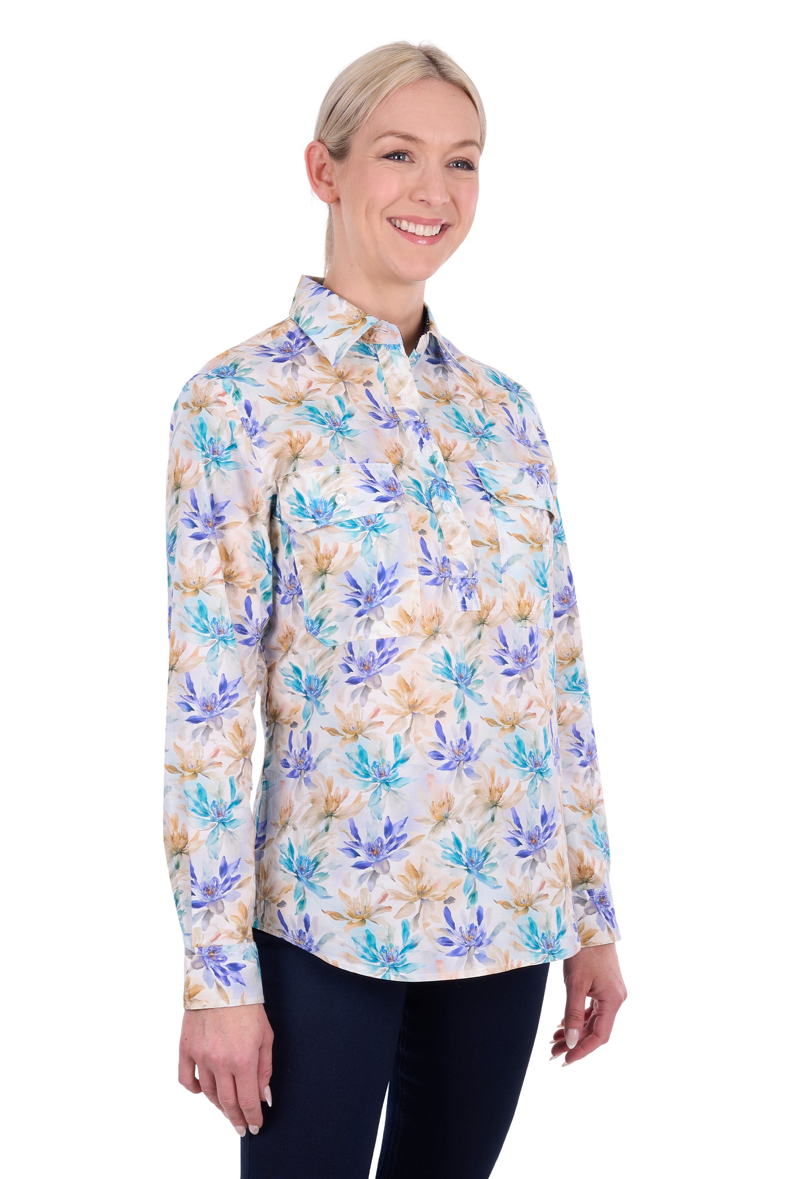 A woman modeling a long-sleeve button-up shirt with a colorful floral print in shades of blue, purple, and beige on a white background, paired with dark navy pants.
