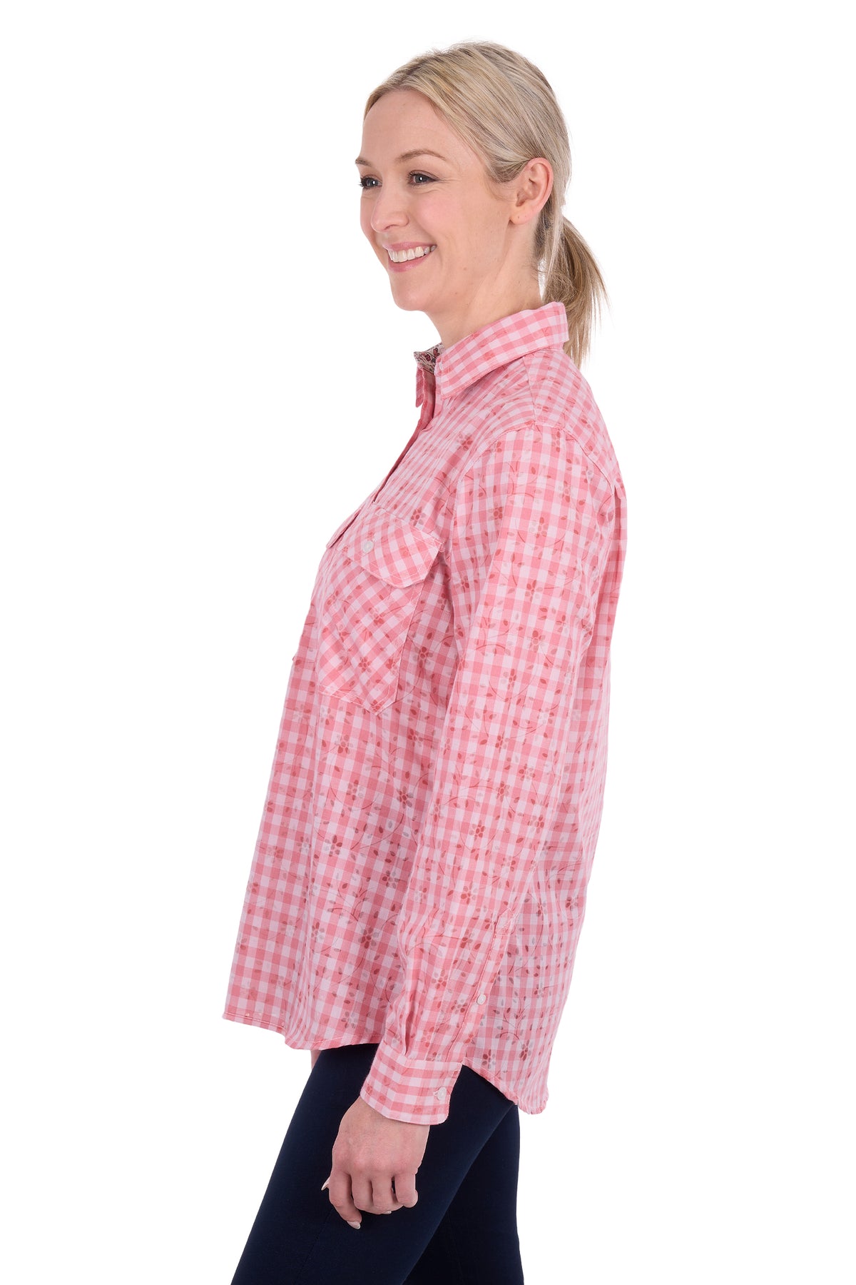 A woman shown in side profile wearing a pink and white gingham long-sleeve button-up shirt and dark pants, photographed against a plain white studio background.