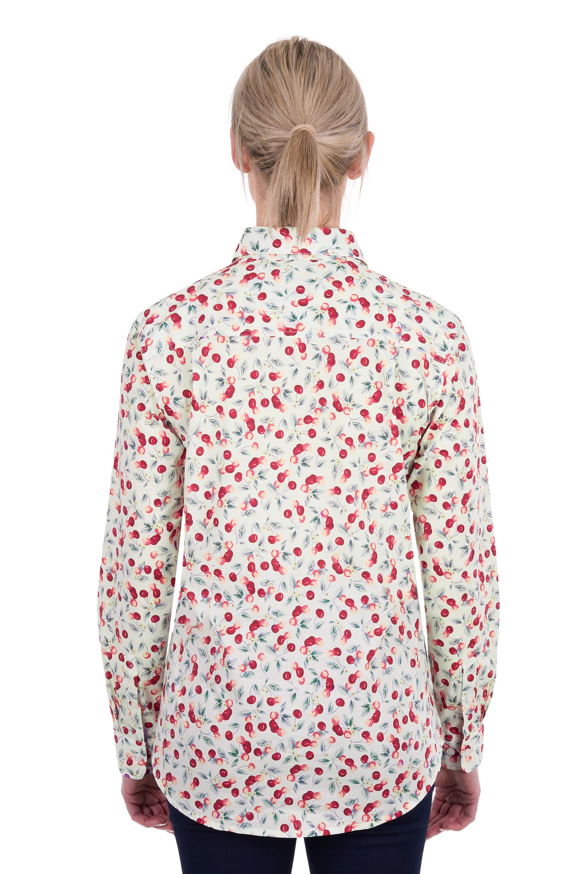 A woman viewed from the back wearing a long-sleeve button-up shirt with a dense red and green cherry print on a white background.