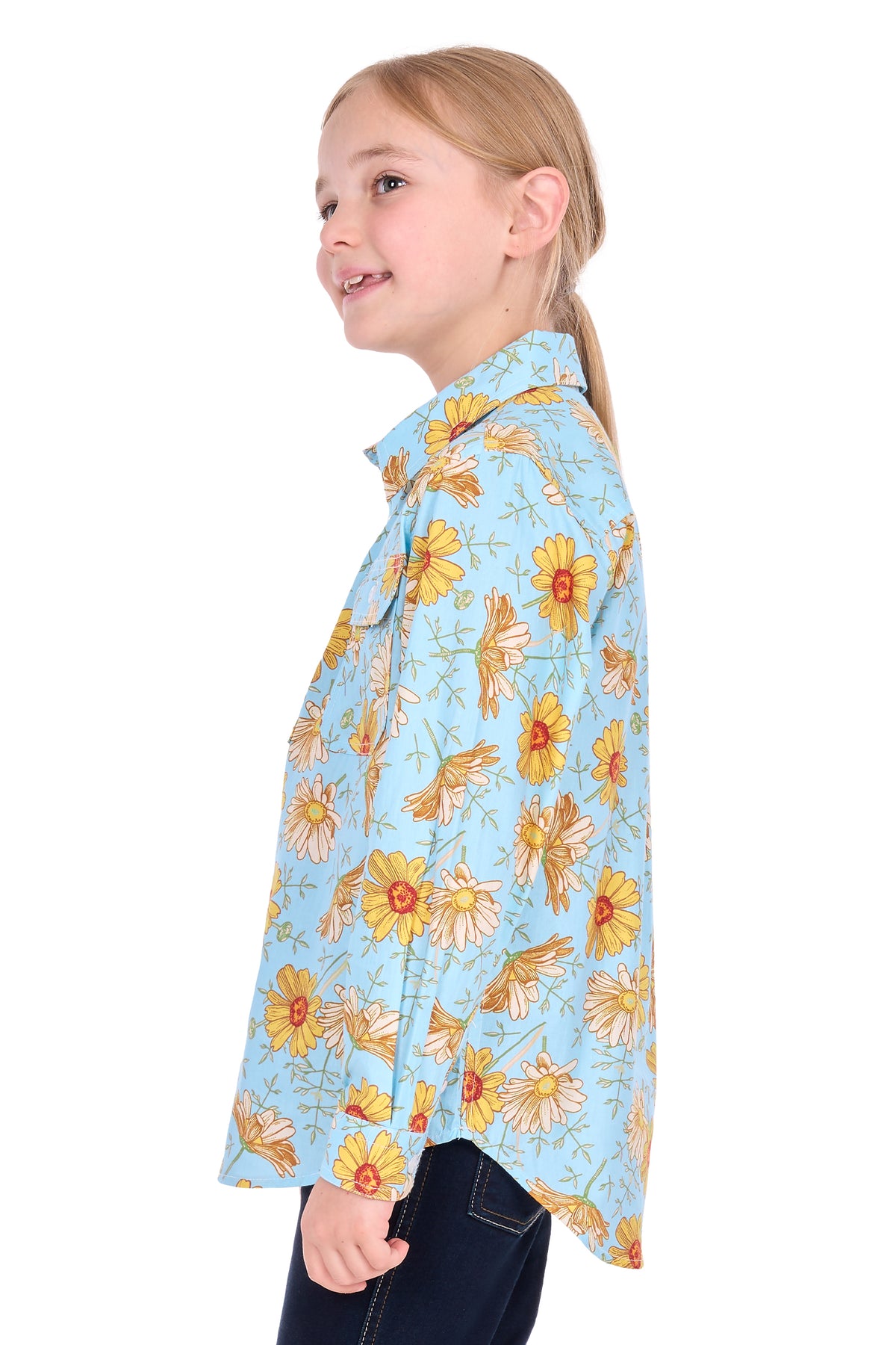 A young girl with blonde hair tied back is shown in profile wearing a light blue button-up shirt with a yellow and orange floral pattern, paired with dark blue jeans, against a plain white background.