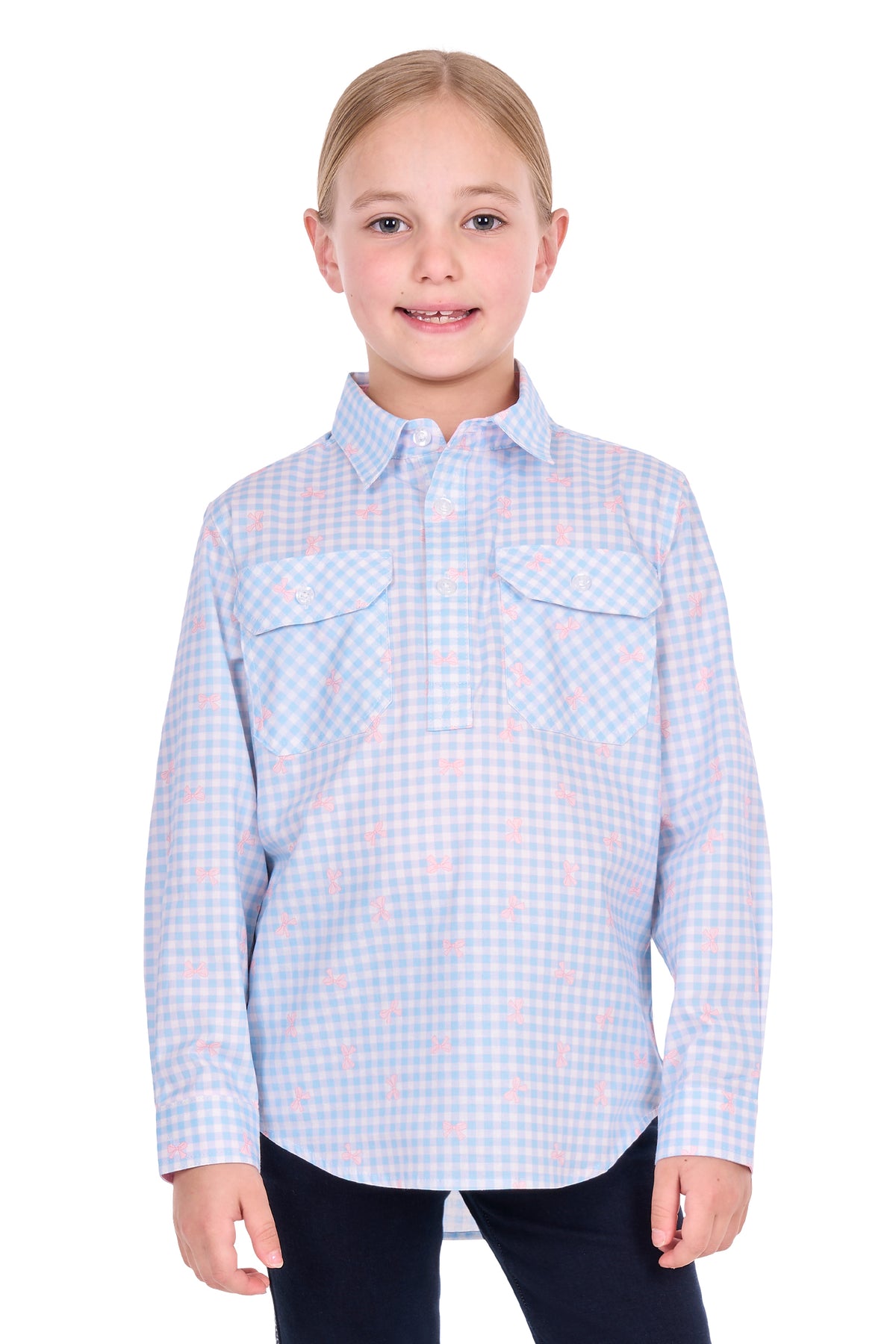 A young girl with blonde hair tied back, wearing a light blue and white gingham long-sleeve button-up shirt with a pink flamingo pattern, paired with dark pants, photographed against a solid white background.