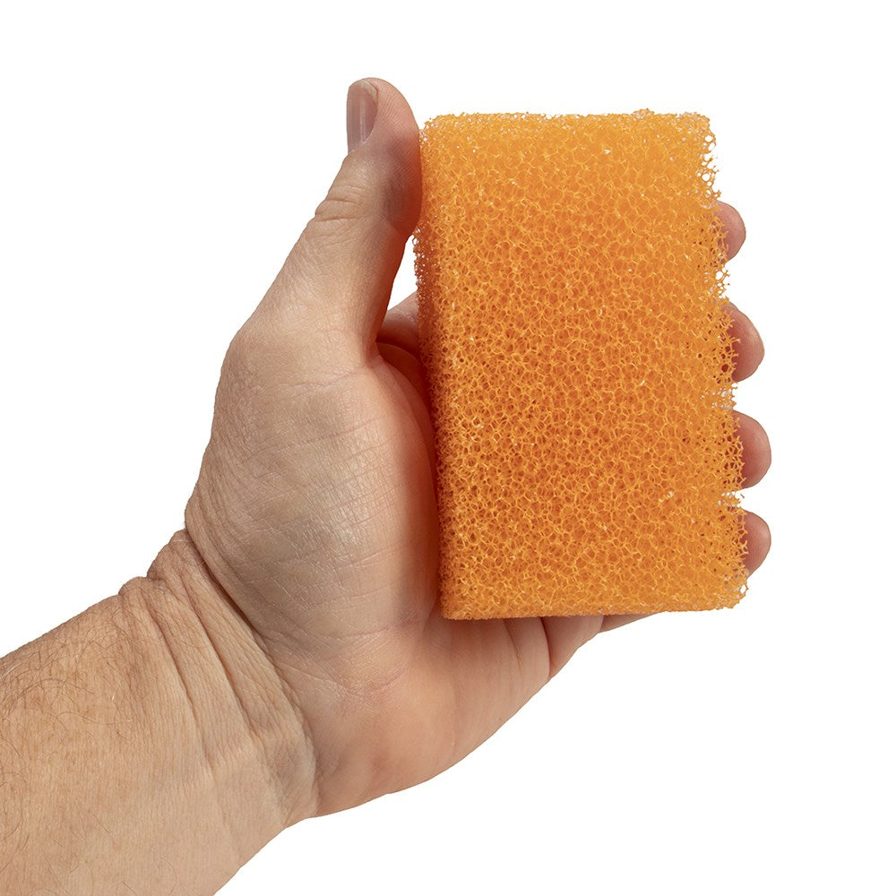 A hand holding a rectangular orange sponge with a porous, foam-like texture against a plain white background.