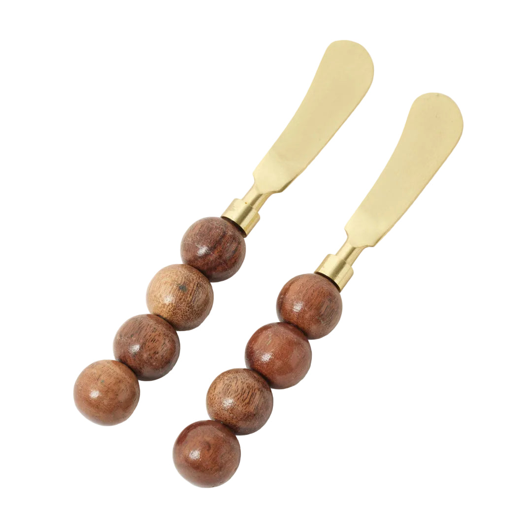 Two gold butter knives with wooden beads on a white background