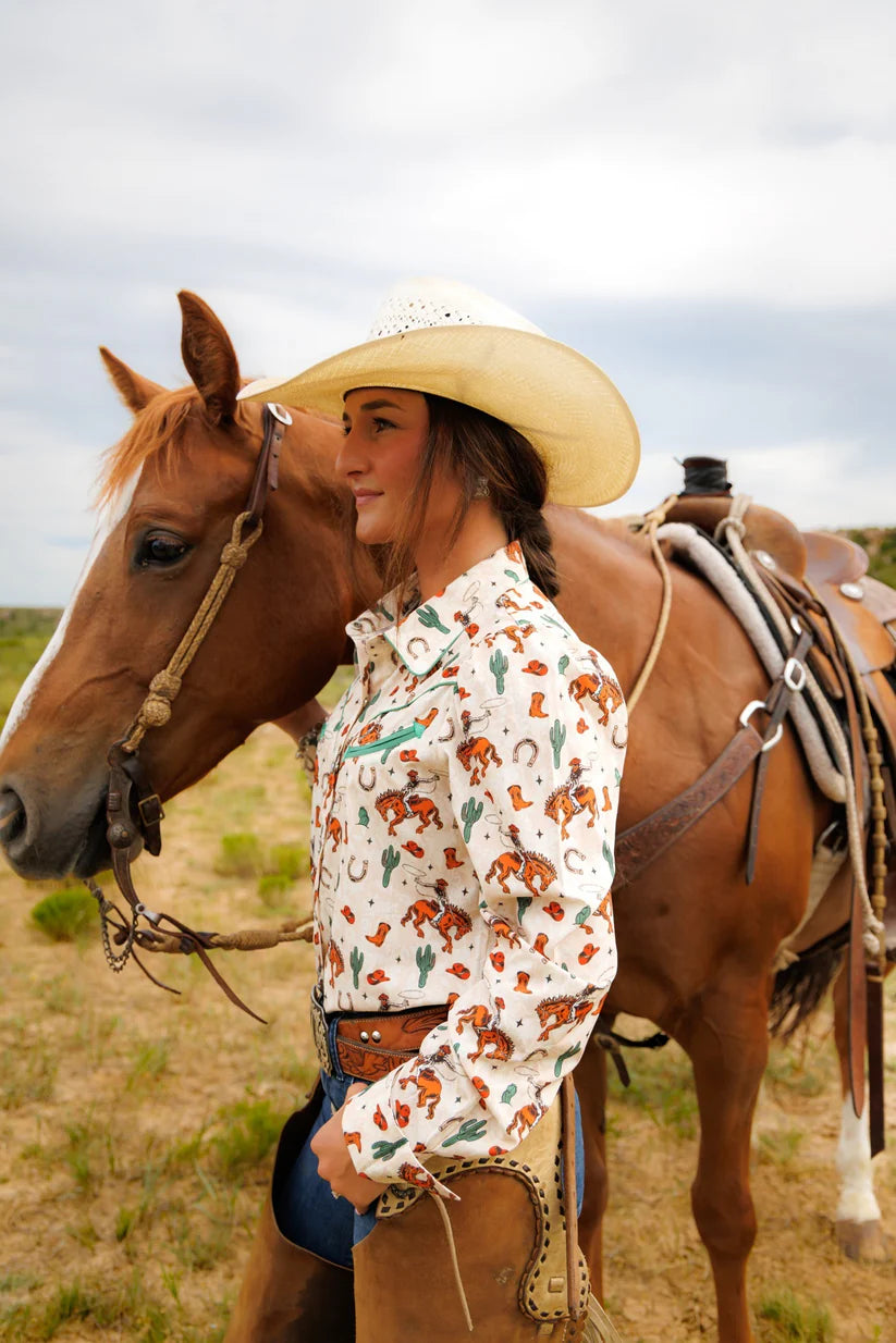 Woman in a patterned shirt and cowboy hat standing next to a horse in an open field.