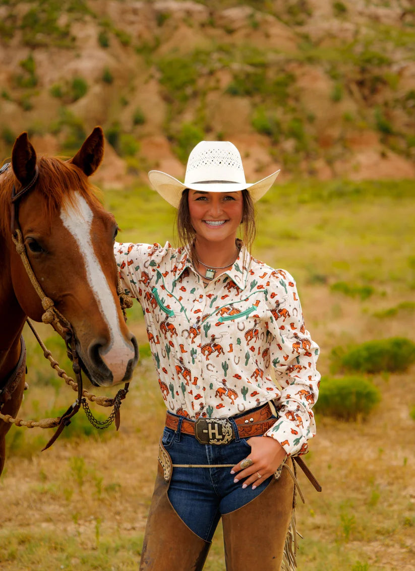 Woman in a patterned shirt and cowboy hat standing next to a horse in a natural setting