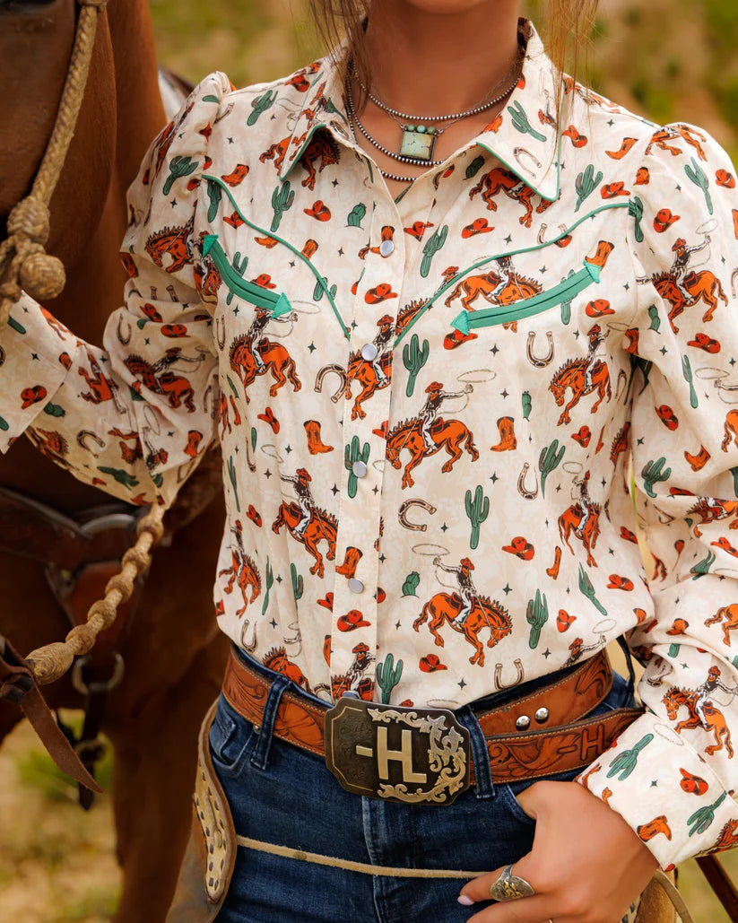 Person wearing a patterned shirt with cowboy design, standing next to a horse.