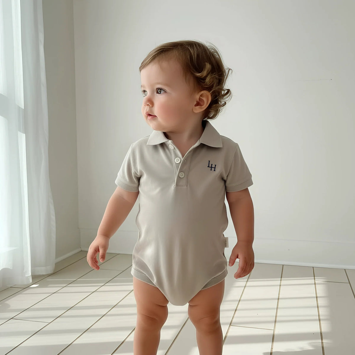 Baby wearing a beige polo shirt with a logo on a white floor and wall background
