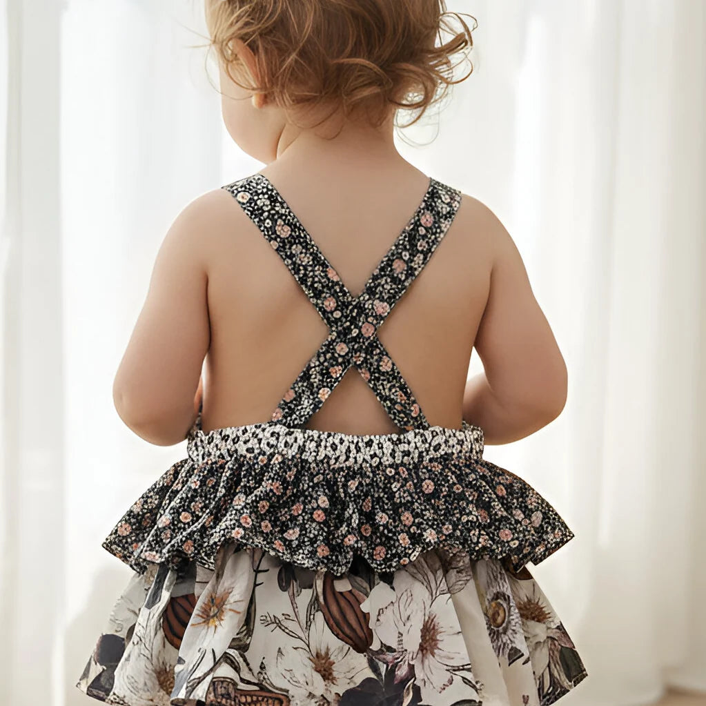 Child wearing a floral dress with criss-cross straps on a white background