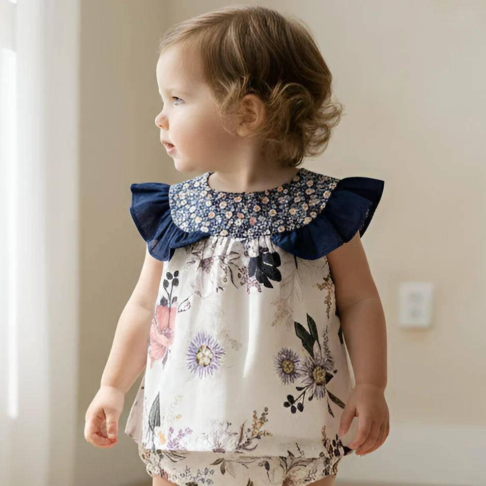 Child wearing a floral dress with ruffled shoulders in a neutral setting