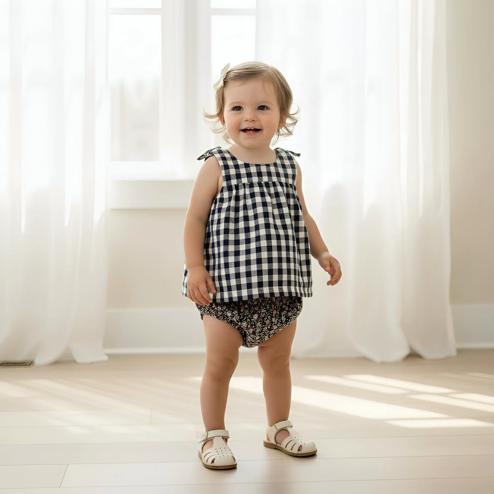 Child wearing a black and white checkered top and floral shorts standing in a bright room with white curtains.