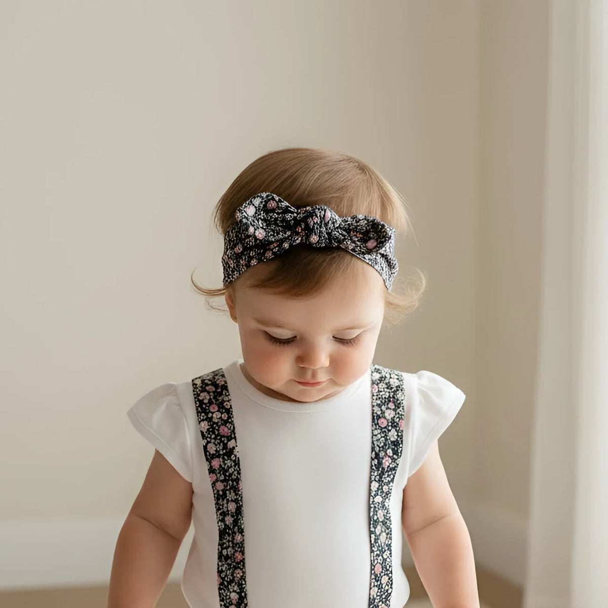 Baby wearing a floral headband and matching outfit against a plain background
