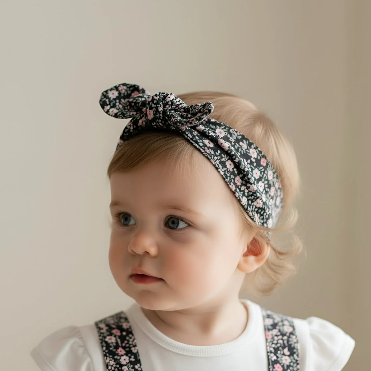 Baby wearing a floral headband and overalls against a beige background