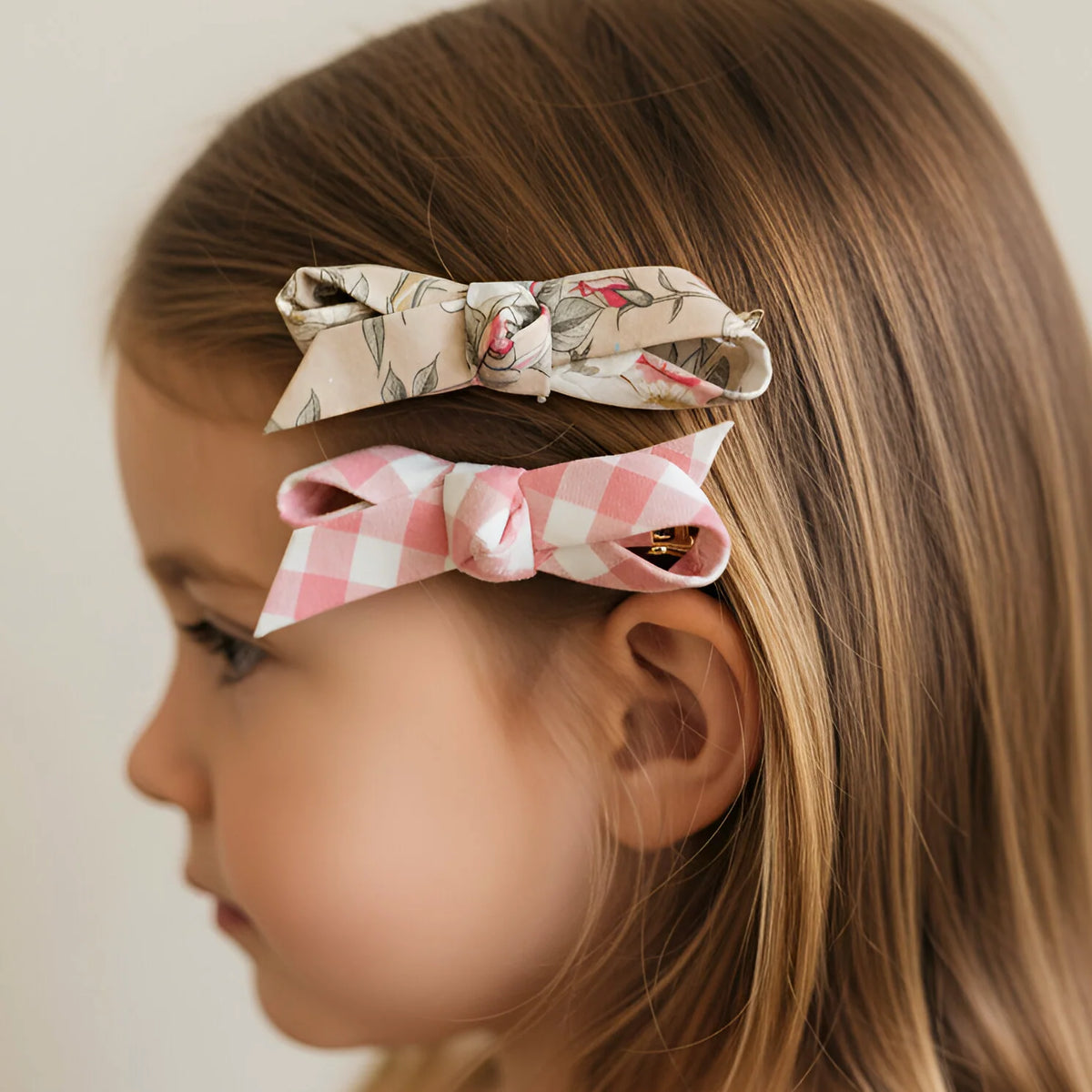 Young girl with floral and checkered hair bows on a plain background