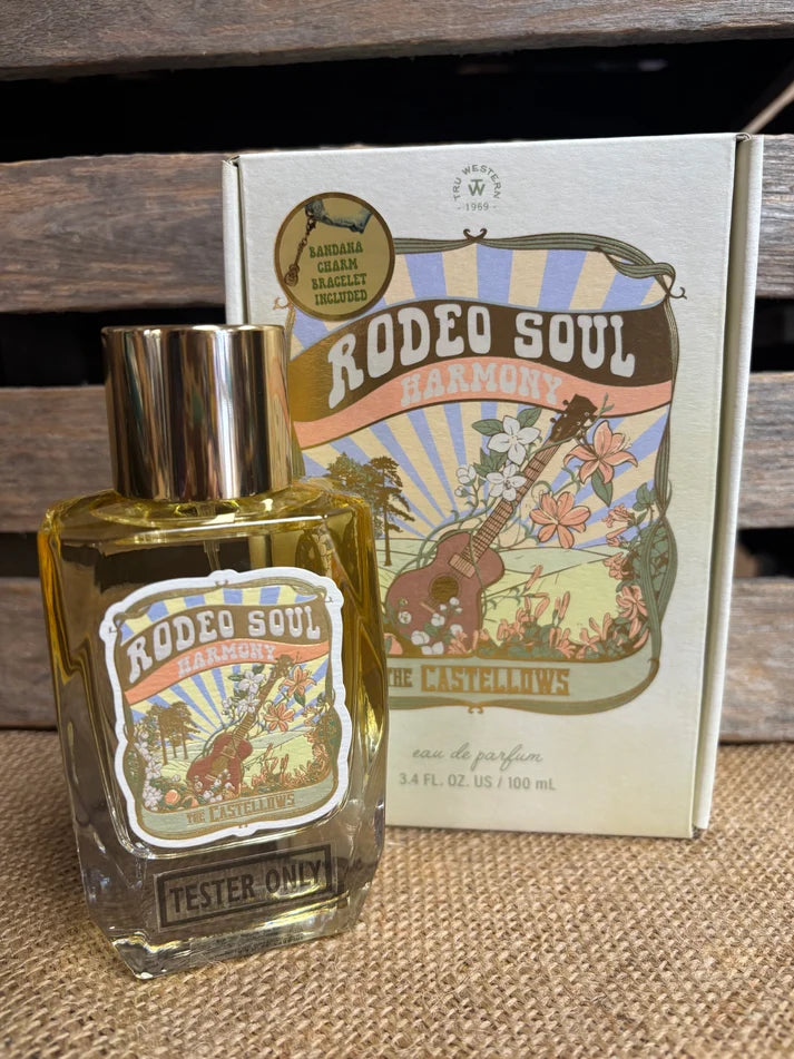 A bottle of Rodeo Soul Harmonie perfume tester with a gold cap stands in front of its illustrated cream-colored packaging box on a burlap surface against a rustic wooden background.