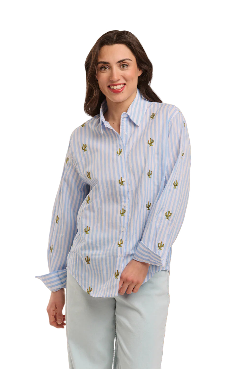 Italian Star Women's Stripe Cactus L/S Shirt. Woman wearing a light blue striped shirt with gold accents against a textured beige wall.