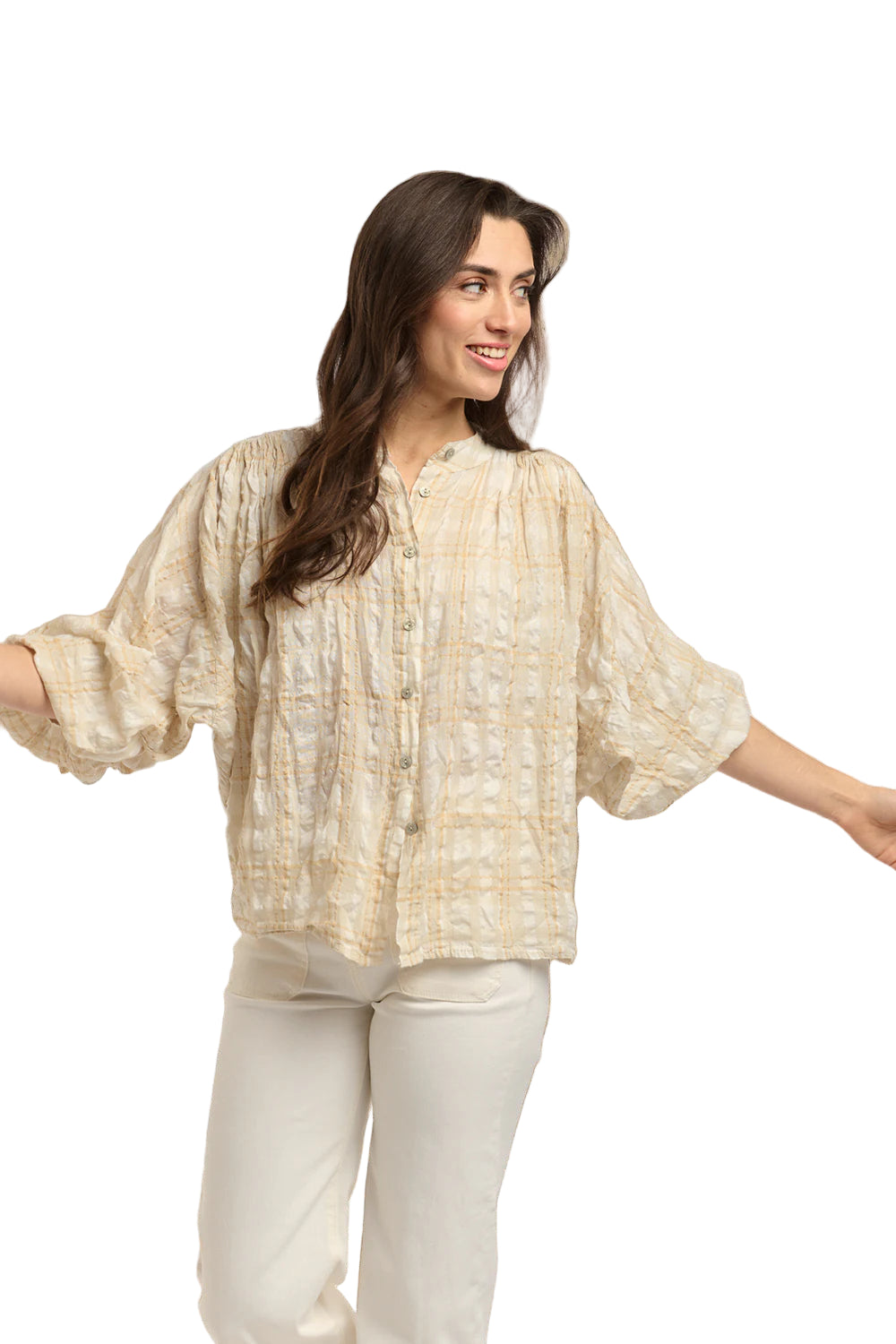 Italian Star Women's Freida Check Shirt. Woman wearing a light-colored blouse with a textured pattern against a stone wall.