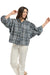 Italian Star Women's Freida Check Shirt. Woman wearing a blue plaid shirt and white pants standing against a stone wall.